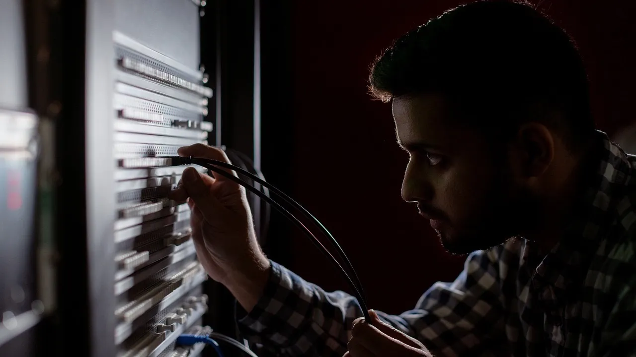 An IT technician closely checks cables on a server rack, so no device goes unwatched.