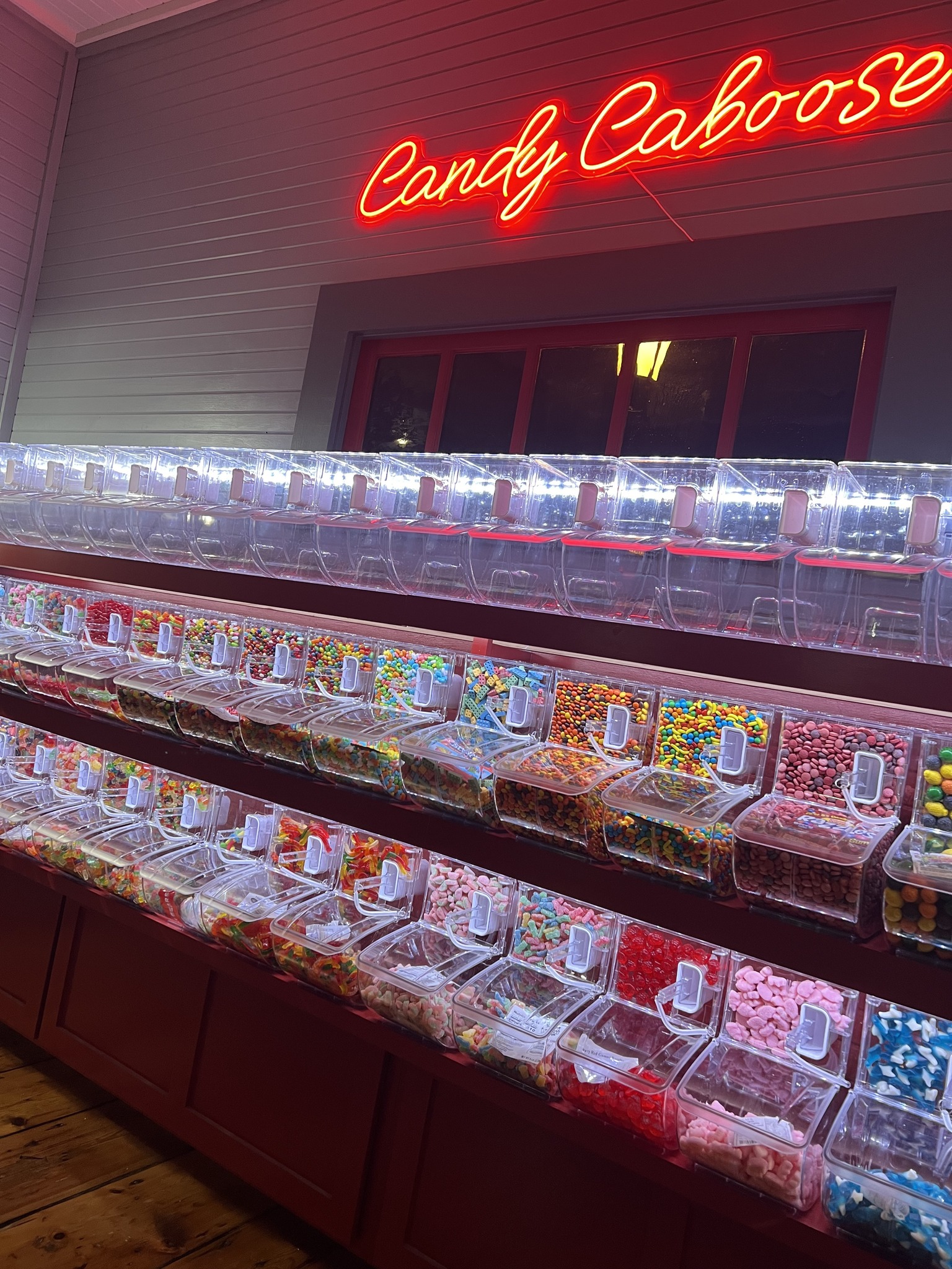 Candy dispenser bins filled with assorted colorful candy under a red neon sign reading Candy Caboose.