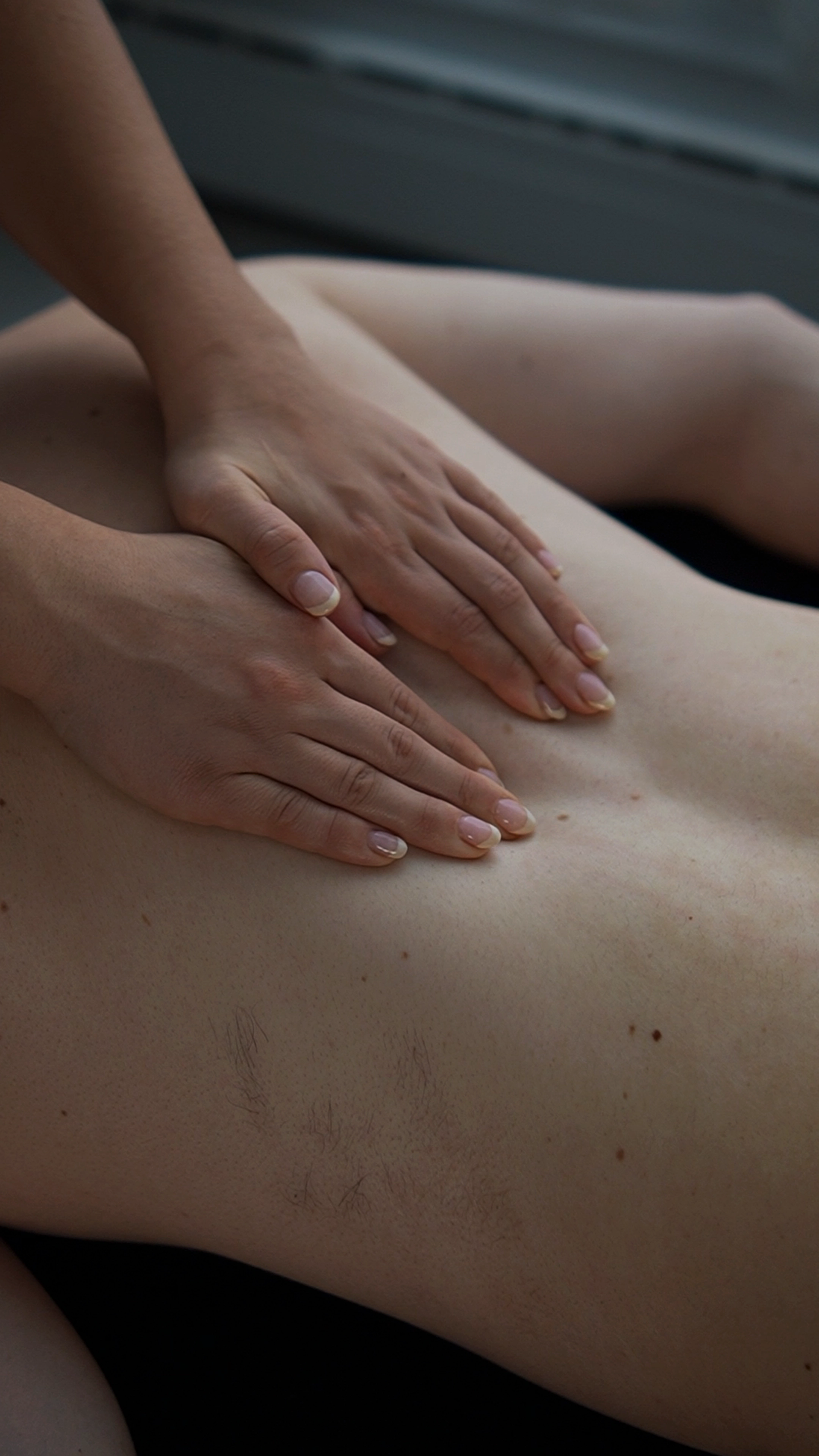 Hands gently pressing on a person's bare back during a massage session.