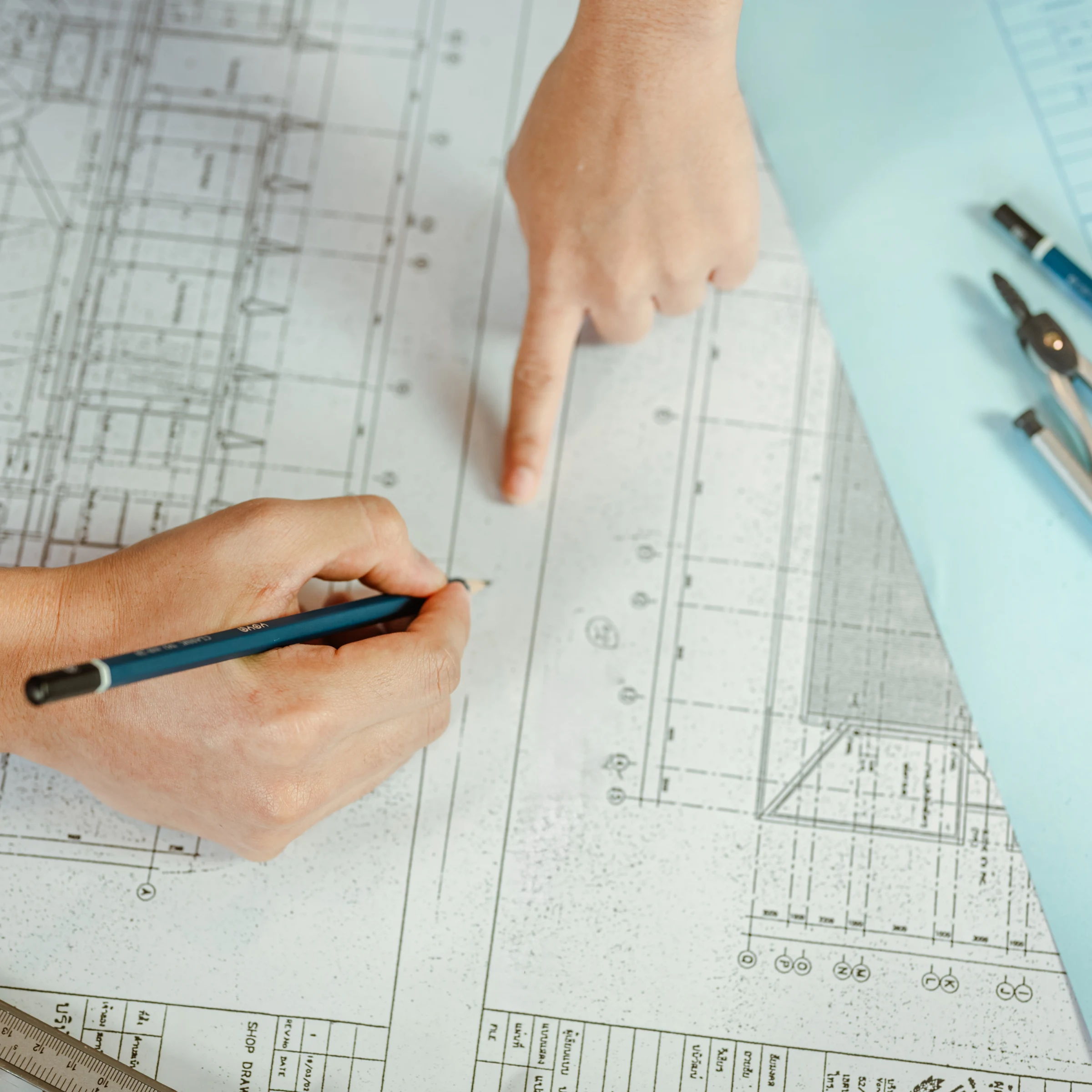 Two hands working on architectural blueprints, one holding a pencil and the other pointing at the plans.