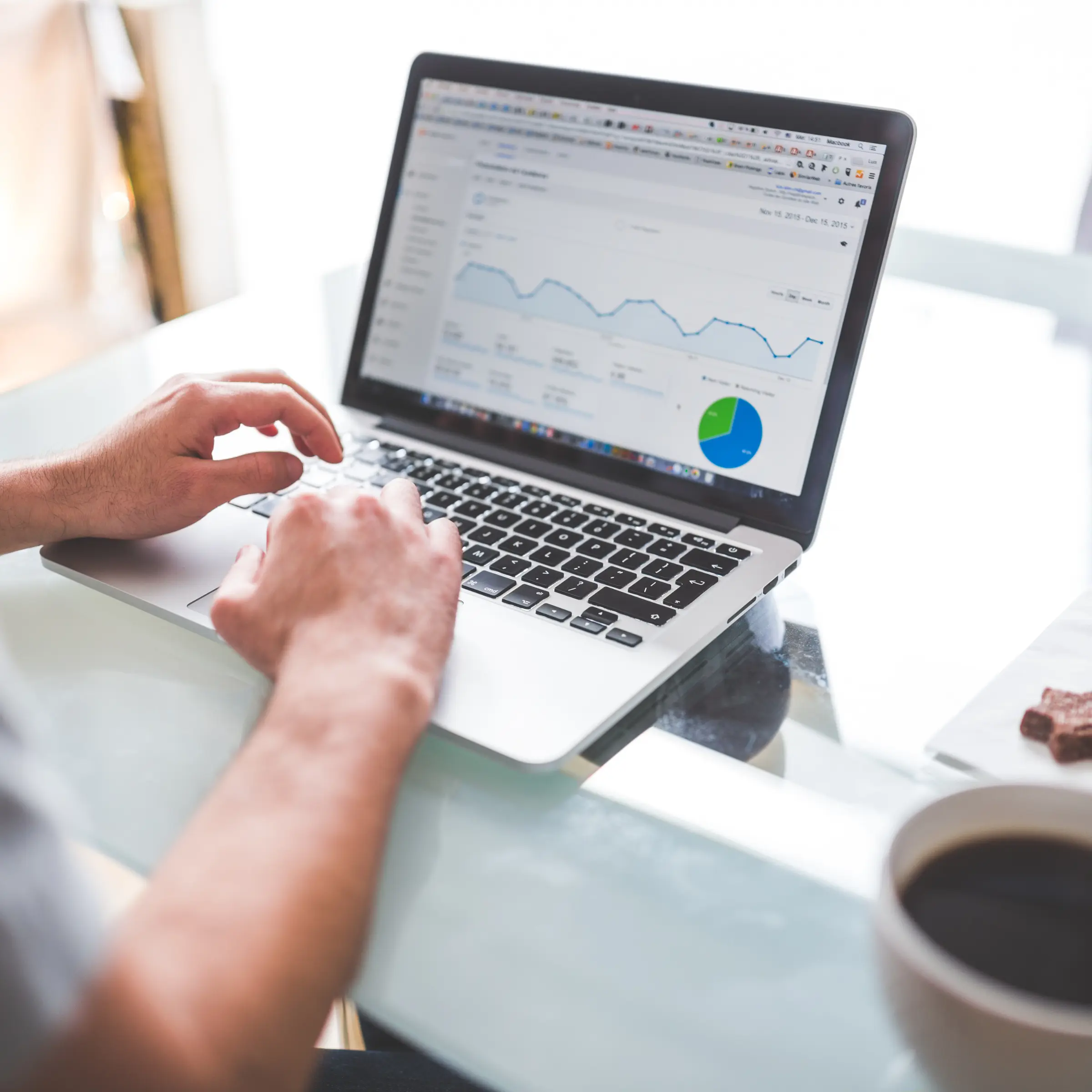 Person typing on a laptop showing website analytics with graphs and a pie chart on screen.