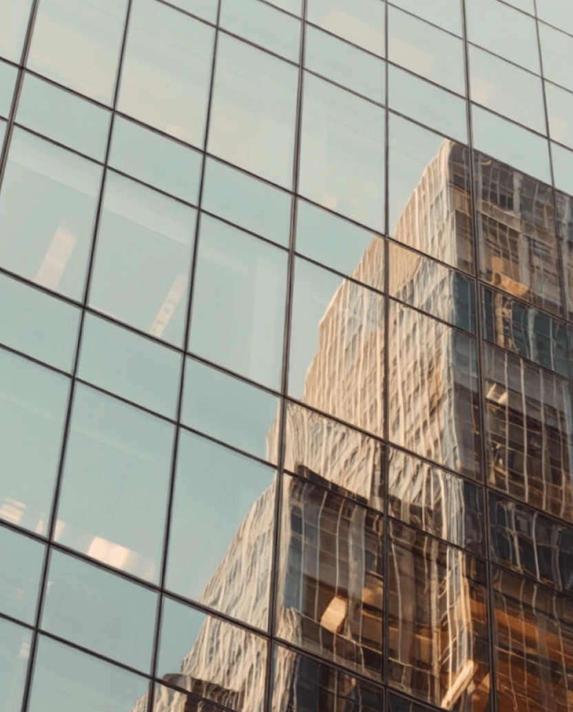 Reflection of a tall building with many windows on the glass facade of another modern skyscraper.