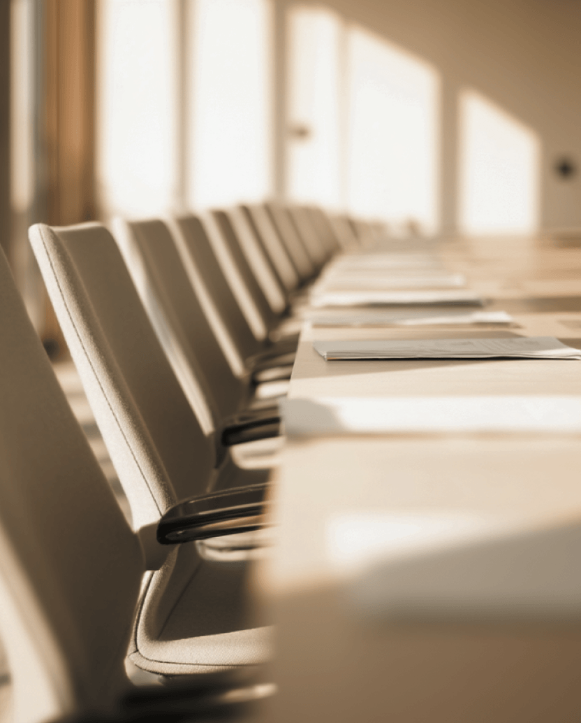 Row of beige office chairs along a conference table with sunlight streaming through windows.