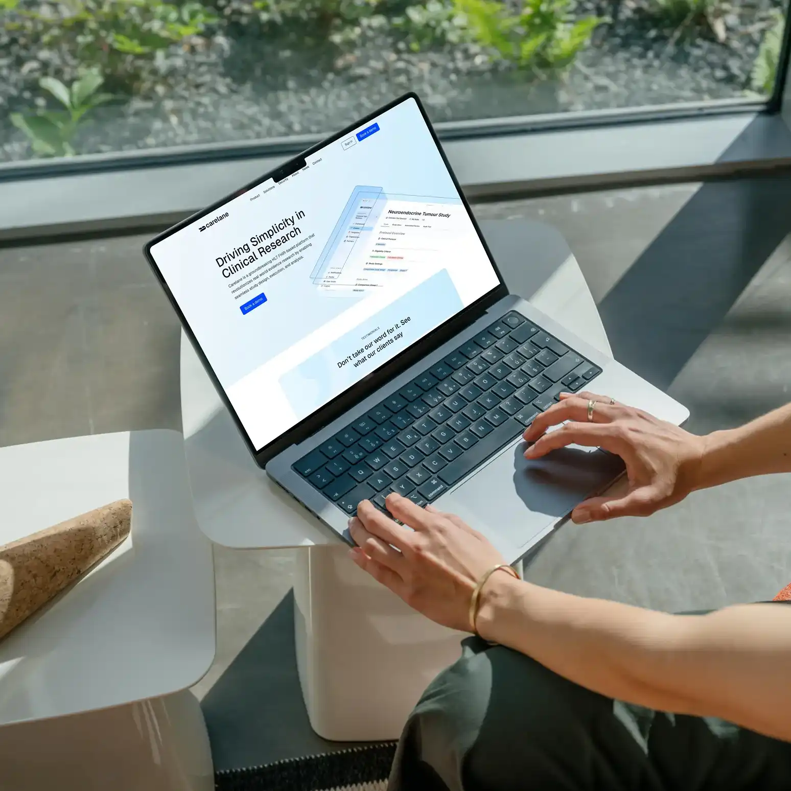 Eine Person tippt auf einem Laptop, der auf einem kleinen weißen Tisch steht, mit einer Website zur klinischen Forschung auf dem Bildschirm.