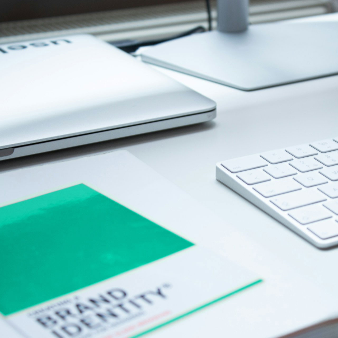 Arbeitsplatz mit geschlossenem Laptop, weißer Tastatur und einem Branding-Identity-Dokument auf einem weißen Tisch.