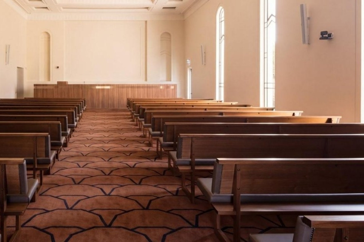 Warm chapel interior with timber pews and patterned carpet leading toward soft window light