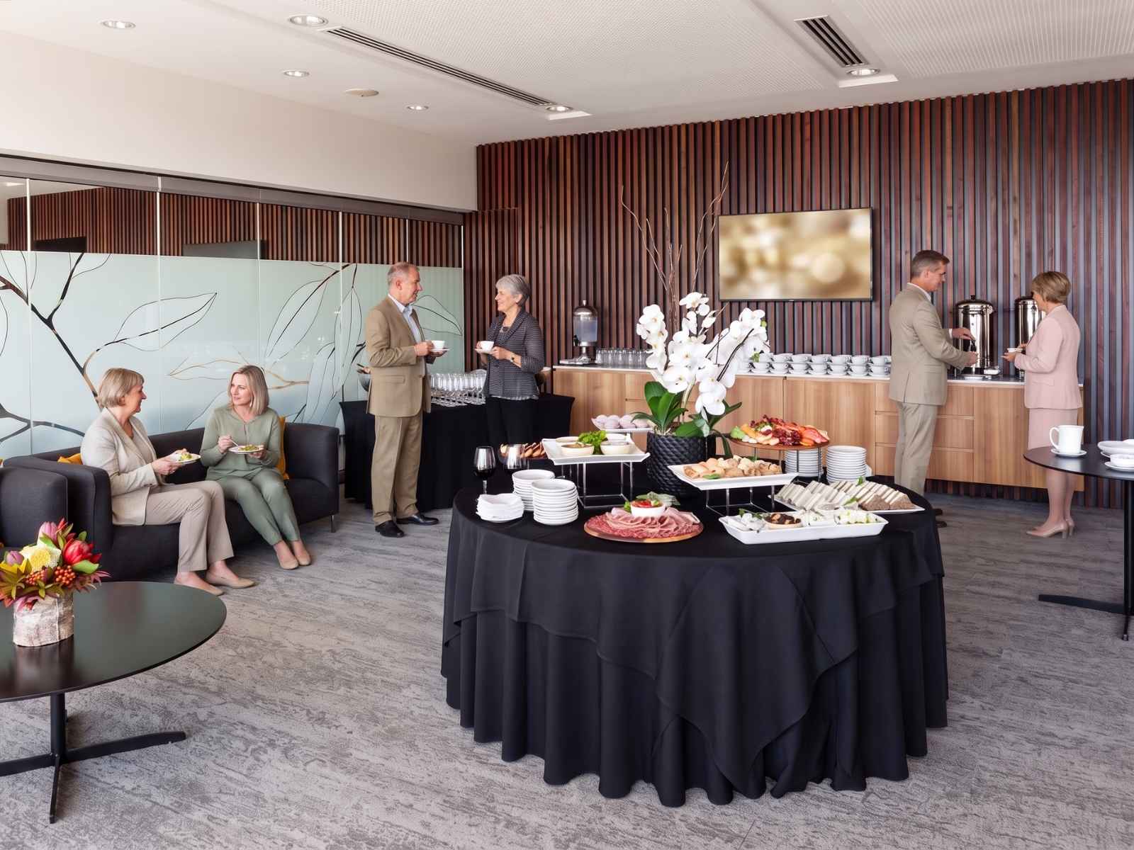 Guests with tea and coffee at a cemetery function centre, food laid out on a black-linen table