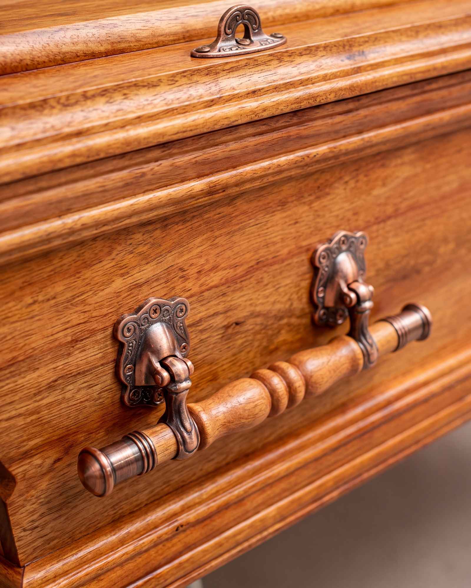 A close detail of the timber grain and copper handle on a coffin