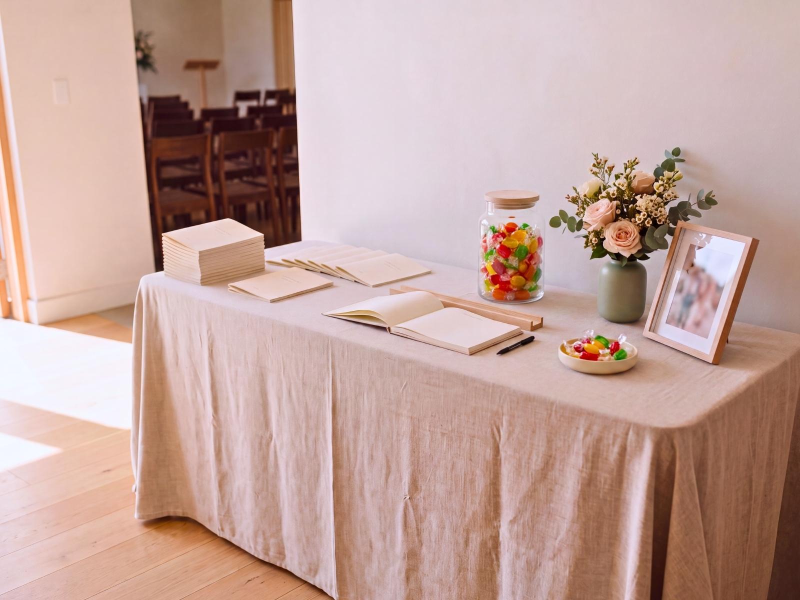 A welcome table with guest book and order of service booklets set before a memorial