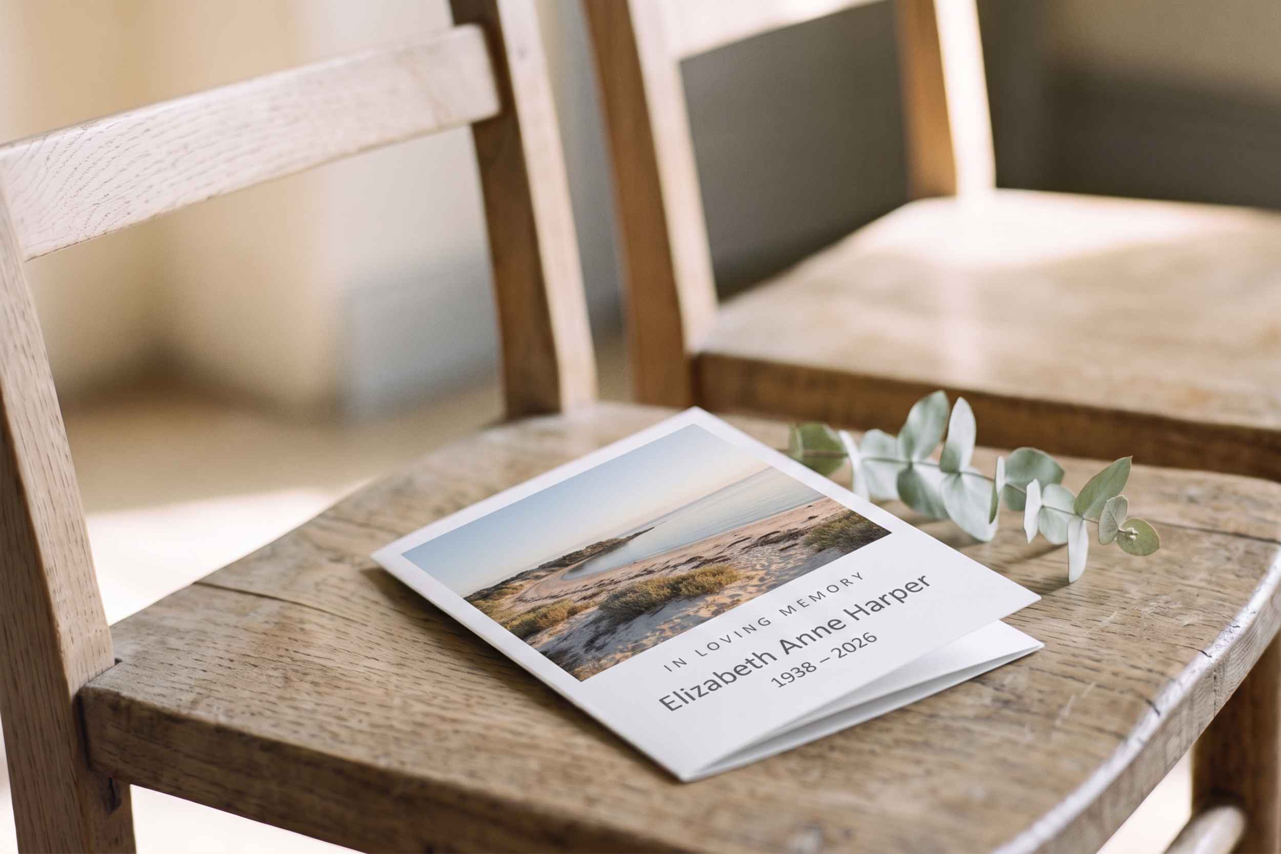 A printed order of service and a sprig of eucalyptus resting on a chair before a service