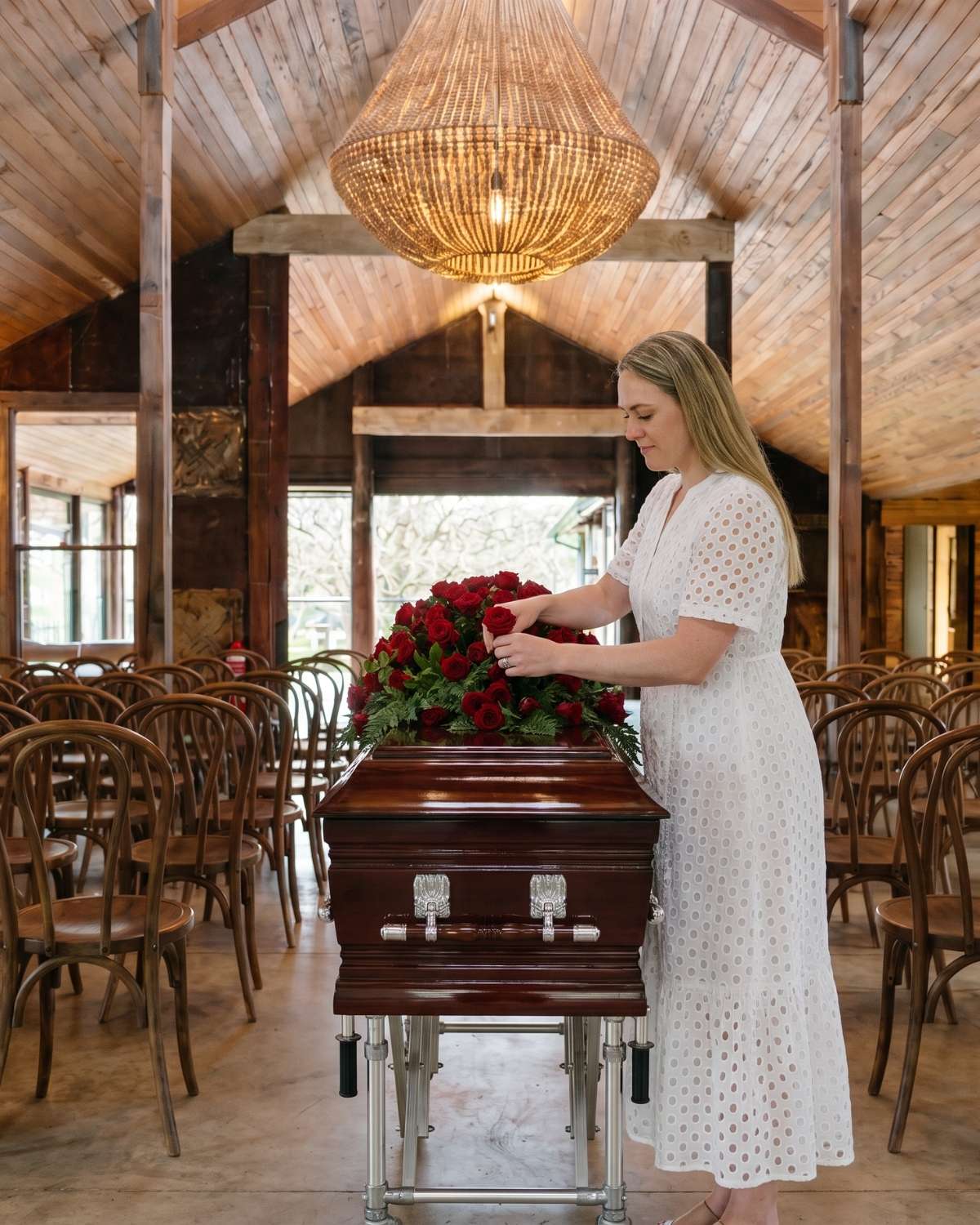 Sameiko gently settling a spray of red roses on a polished mahogany casket in the barn venue
