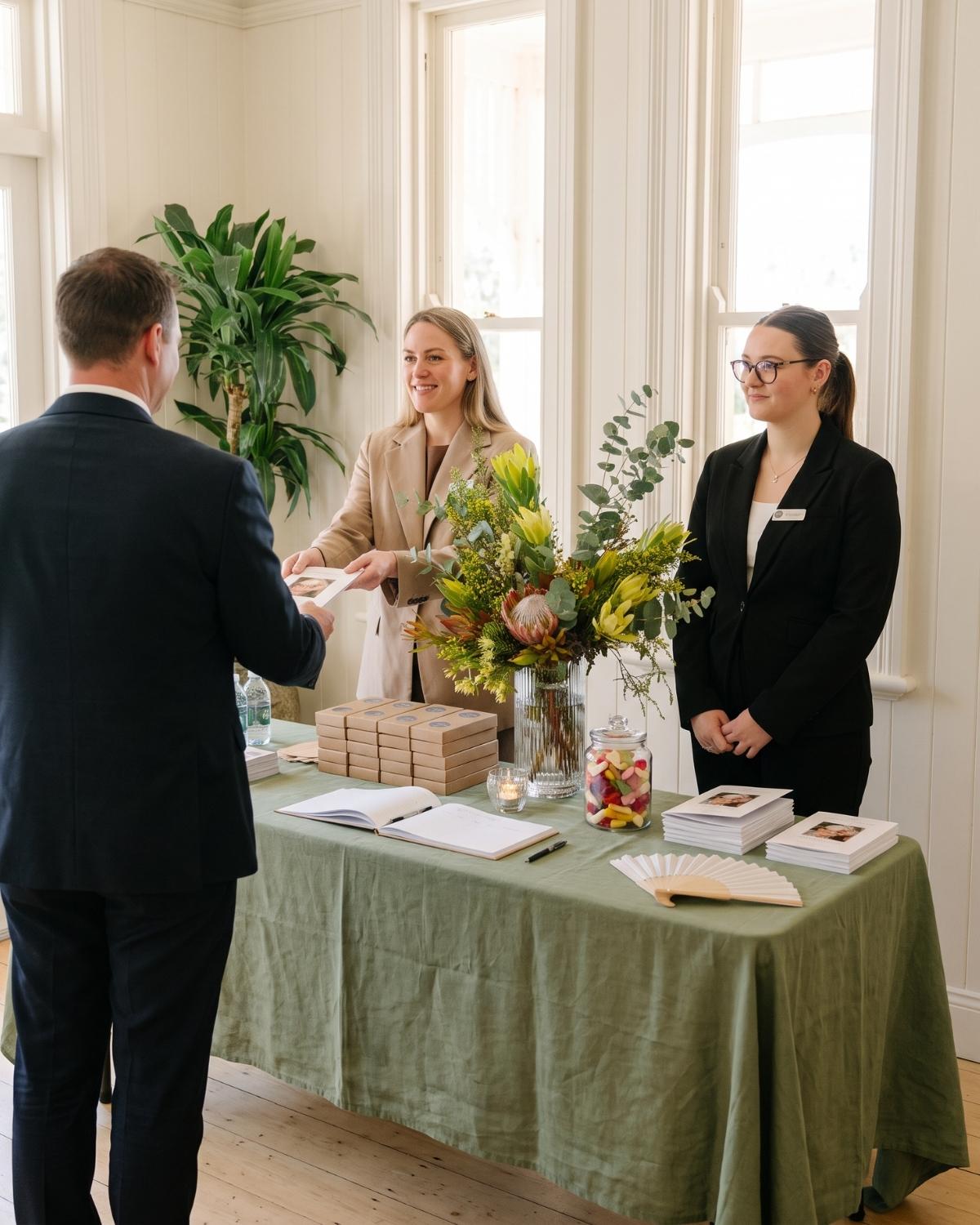 Sameiko and Mackenzie welcoming a guest at the arrival table with an order of service