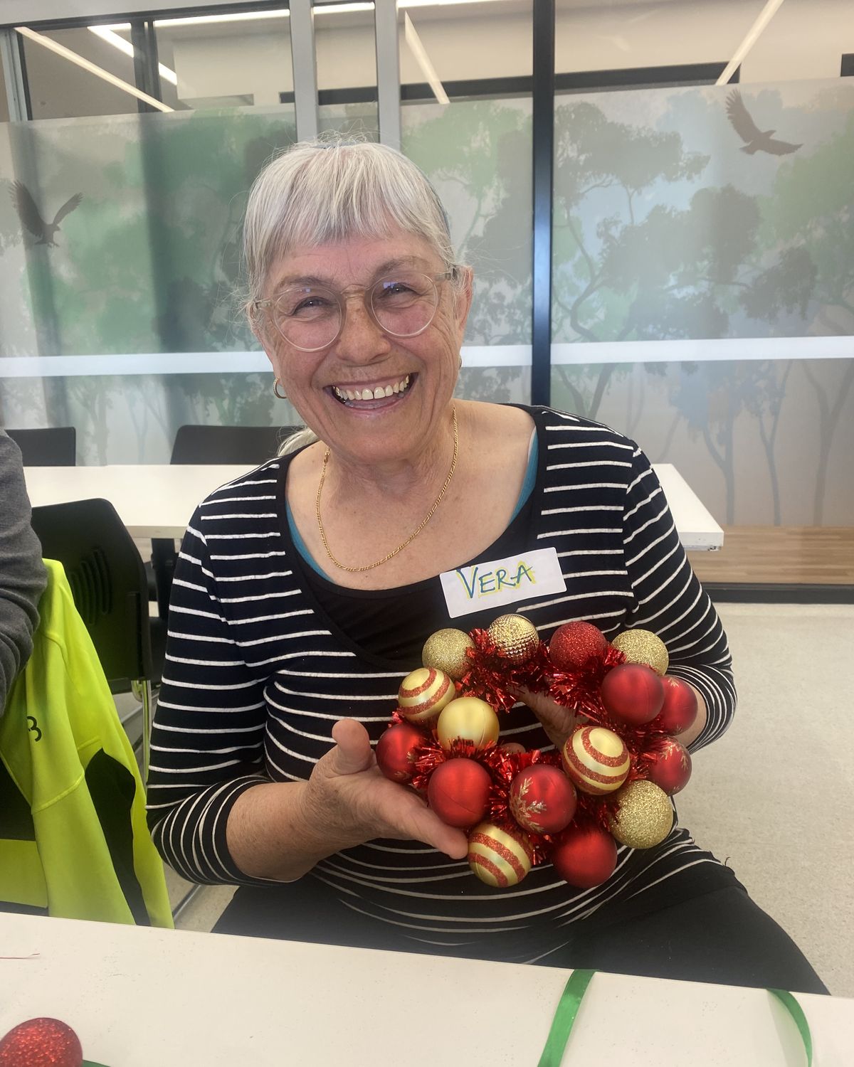 Vera laughs as she holds up the red and gold bauble wreath she made at Candour Connects