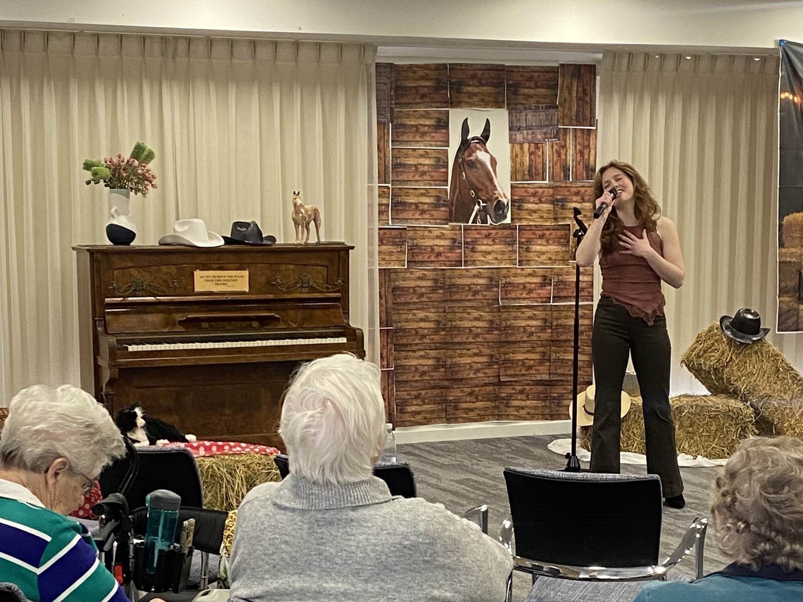 A singer performs beside an upright piano for residents at a local aged care home