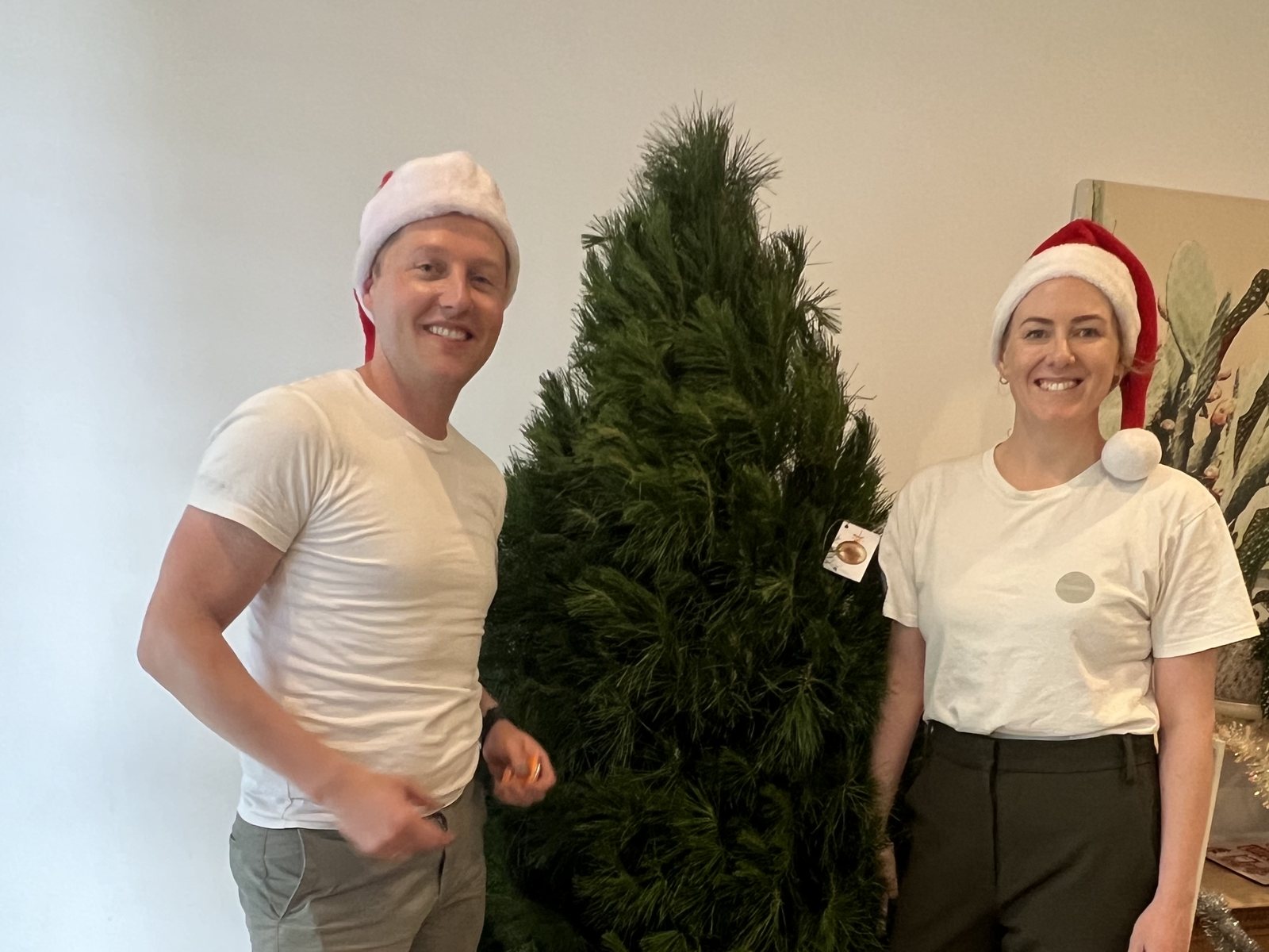 Two of the Candour team in Santa hats beside a real Christmas tree delivered to a retirement home
