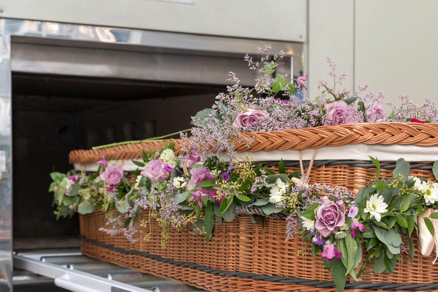 A willow coffin dressed with flowers moving into a cremator