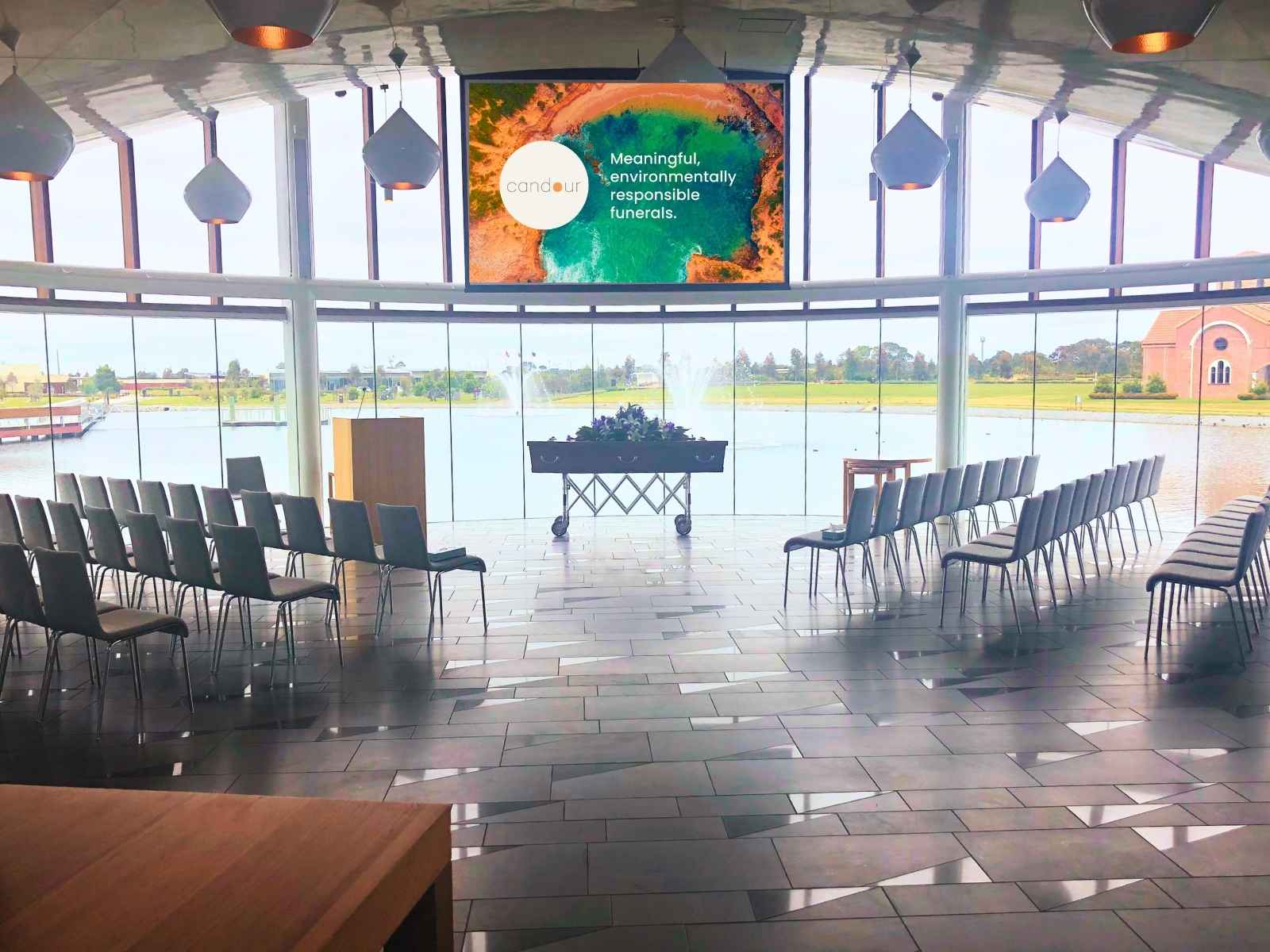 Candour Funerals on screen with coffin present at Sanctuary Chapel looking out to lake through glass windows