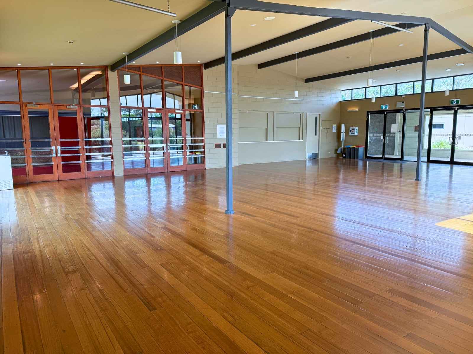 A wide, open space with timber floors, a bank of glass doors and windows, and exposed beams, ideal for receptions or community gatherings.