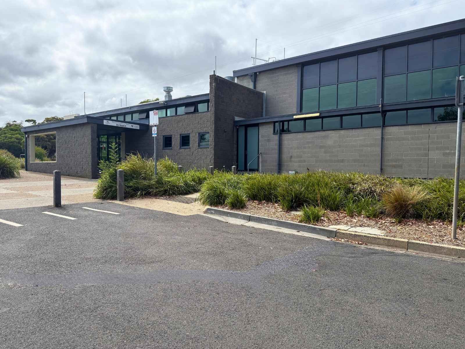 The modern grey exterior of Peninsula Community Theatre as seen from the adjacent car park, with landscaped gardens, signage, and a clear view of the entrance.