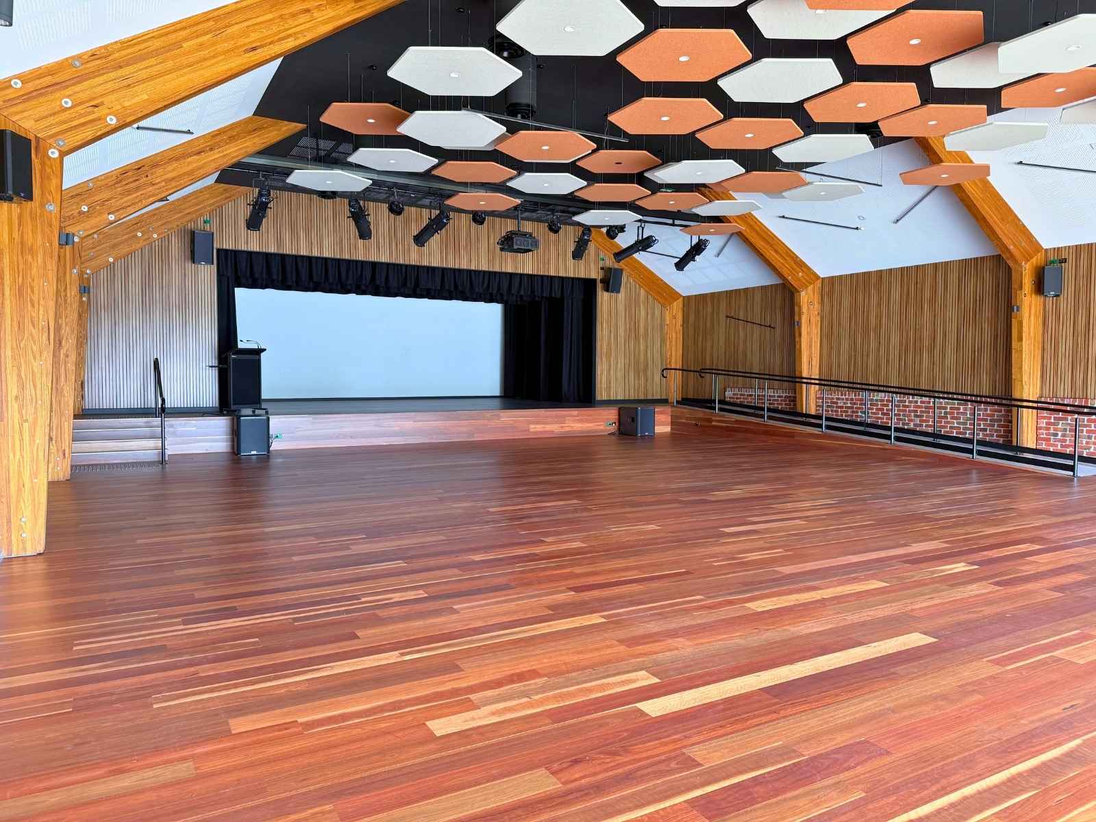 A spacious hall with polished timber floors, natural wood beam accents, and a large presentation stage, offering flexibility for events, services, or performances.
