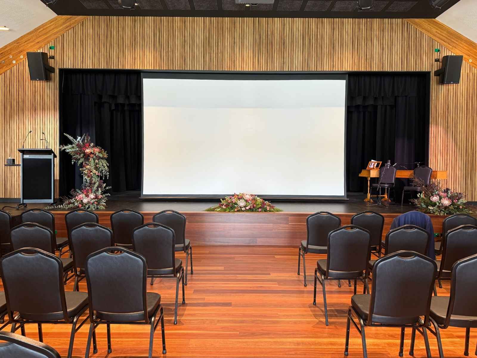 A close-up of the stage setup with a lectern, screen, and floral arrangements in soft pinks and greens, creating a respectful setting for a memorial or presentation.