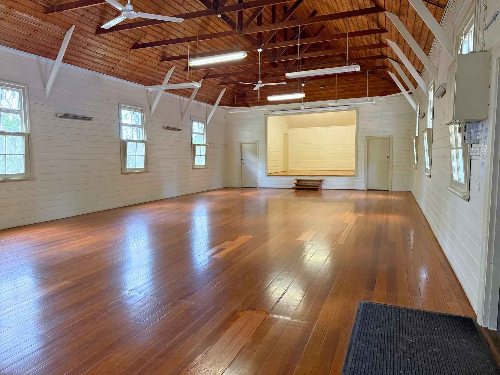 A wide, empty space inside the Mechanics Hall, highlighting polished wooden floors, white timber walls, and exposed ceiling beams under warm, diffused lighting.