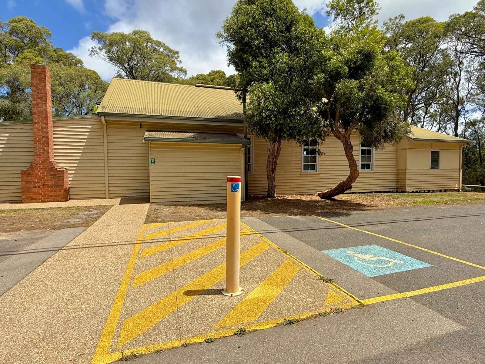 A clear view of the front of Red Hill Mechanics Hall, showing ramp access, a brick chimney, and a designated accessible parking space surrounded by native trees.