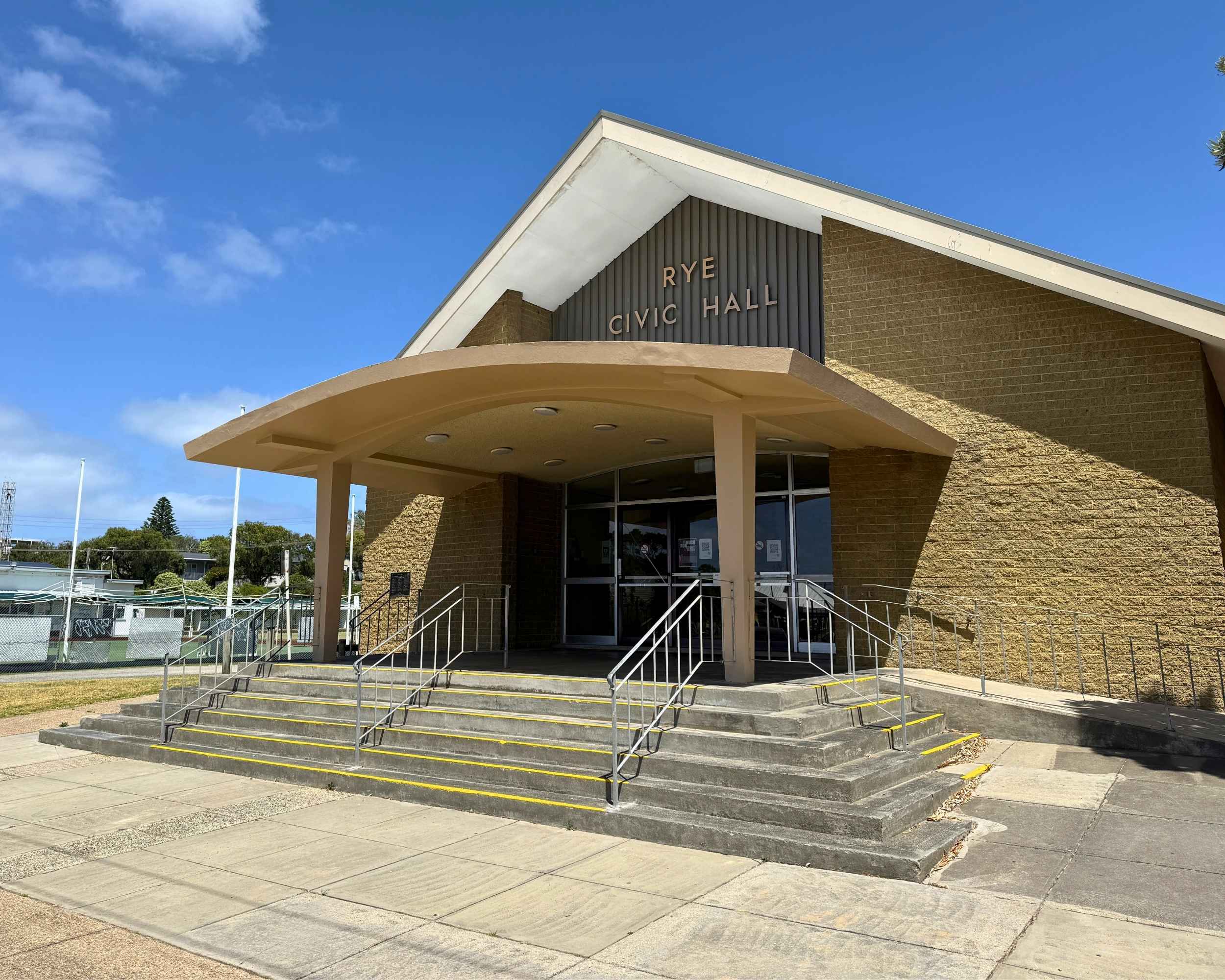A mid-century style brick civic hall with a pitched roof and wide front steps leading to glass entrance doors under a curved canopy.