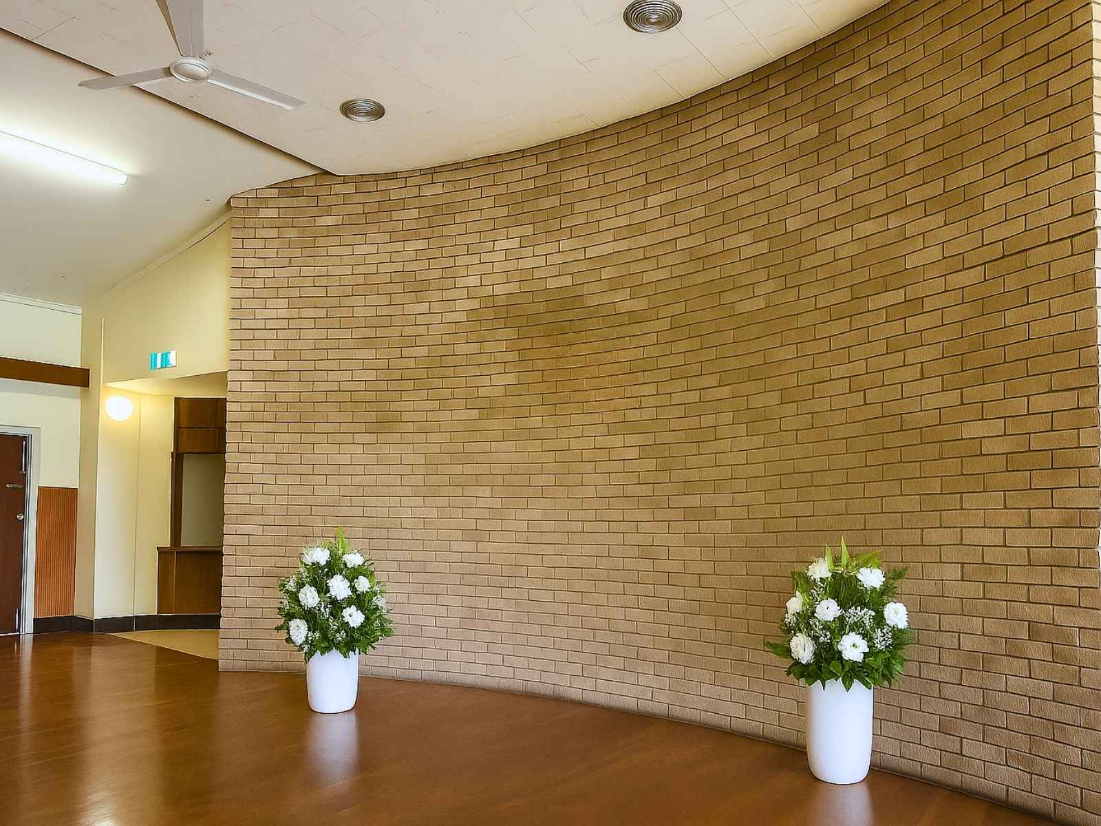 Two white vases of flowers placed before a curved exposed brick wall, creating a simple and respectful setting for a memorial service.