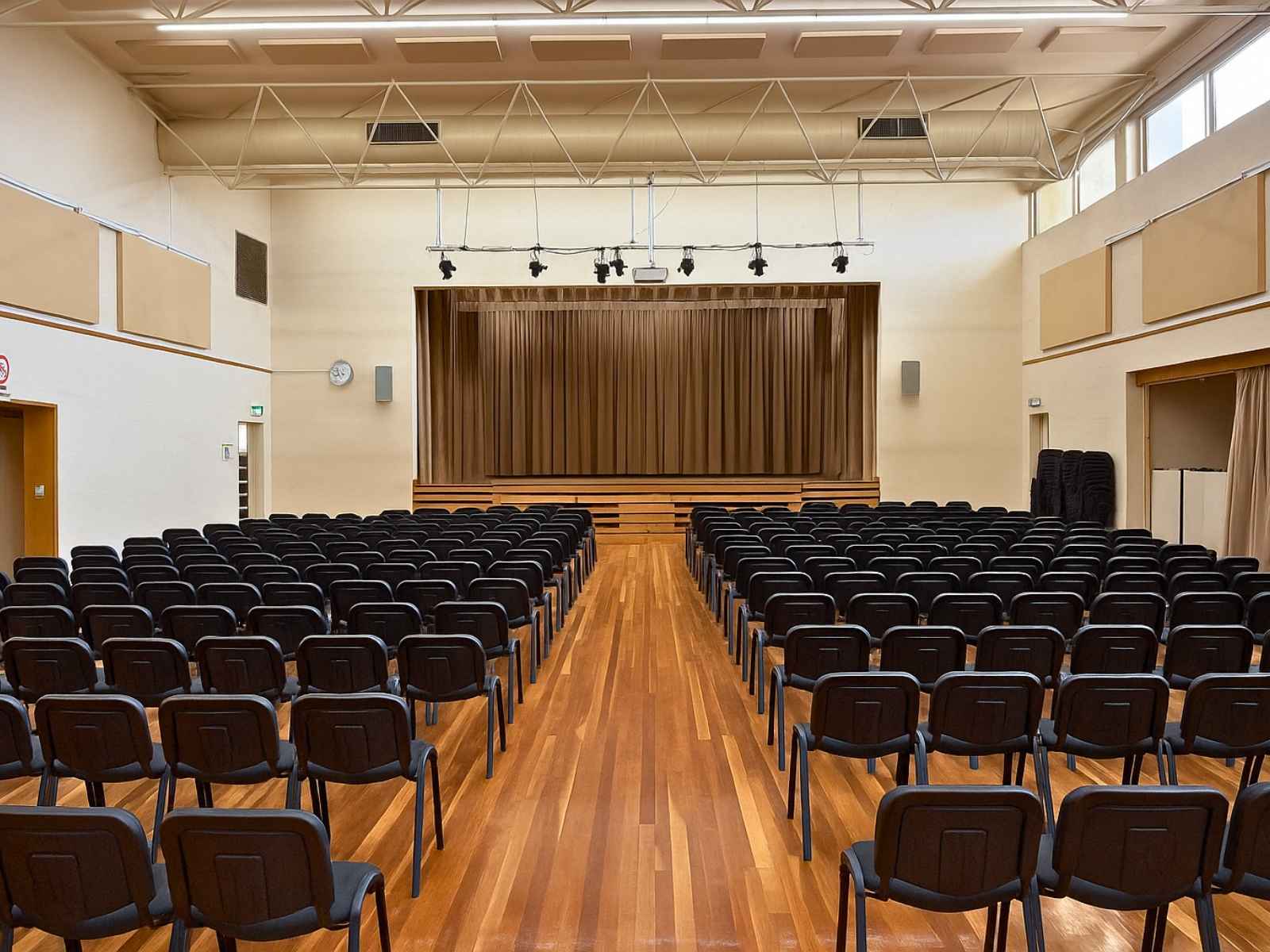 Theatre-style seating with black chairs facing a curtained stage.