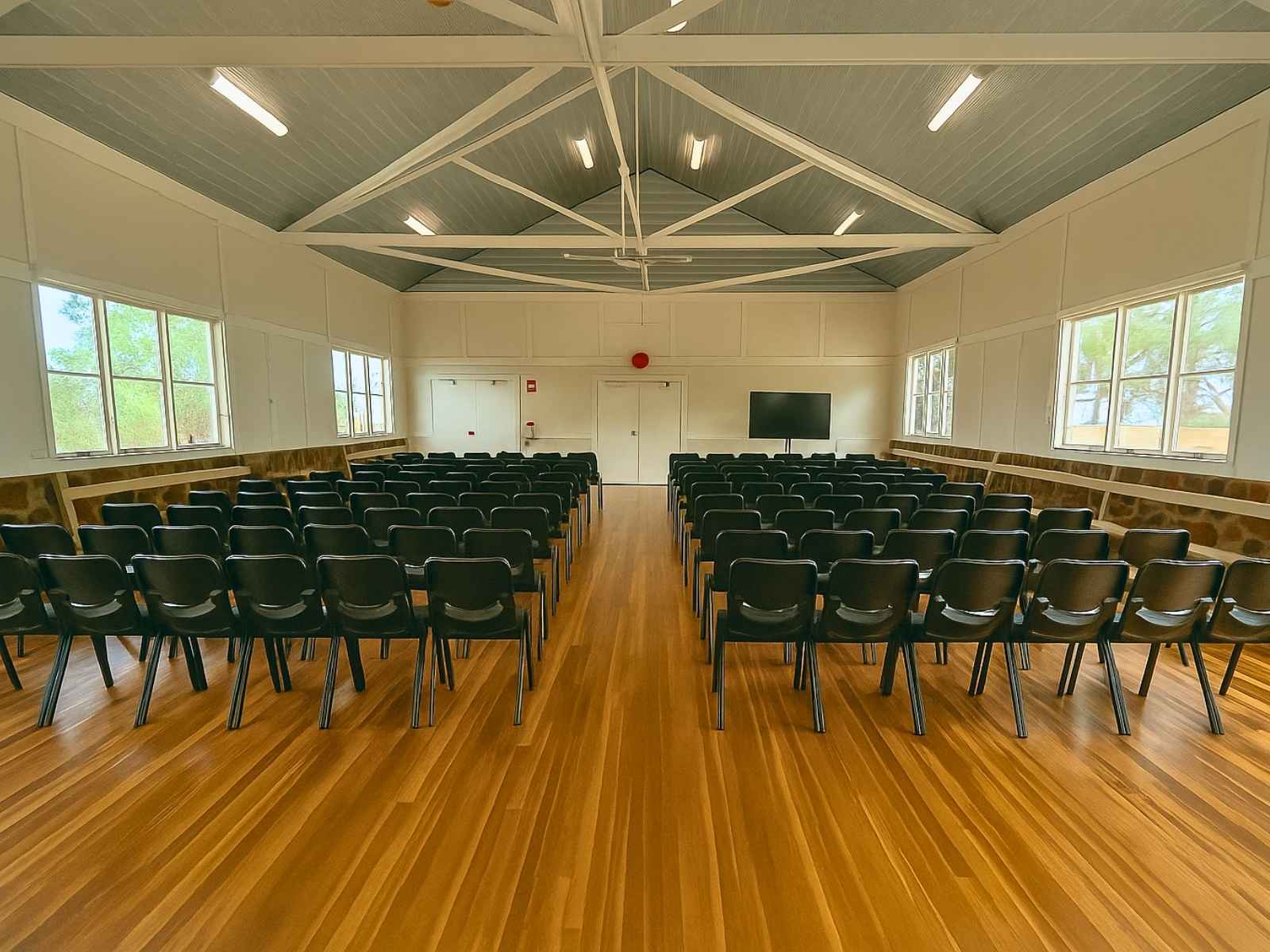 Reverse angle of the interior showing seating arrangement facing the hall’s front wall, with large windows allowing natural light to fill the space.