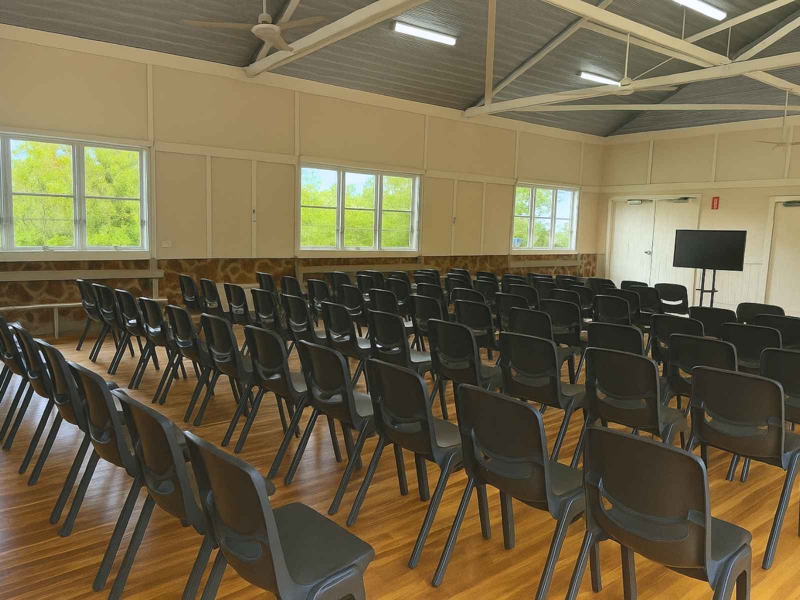 Interior shot of the hall set up for a seated event, with rows of black plastic chairs on polished timber floors beneath a high vaulted ceiling with exposed beams.