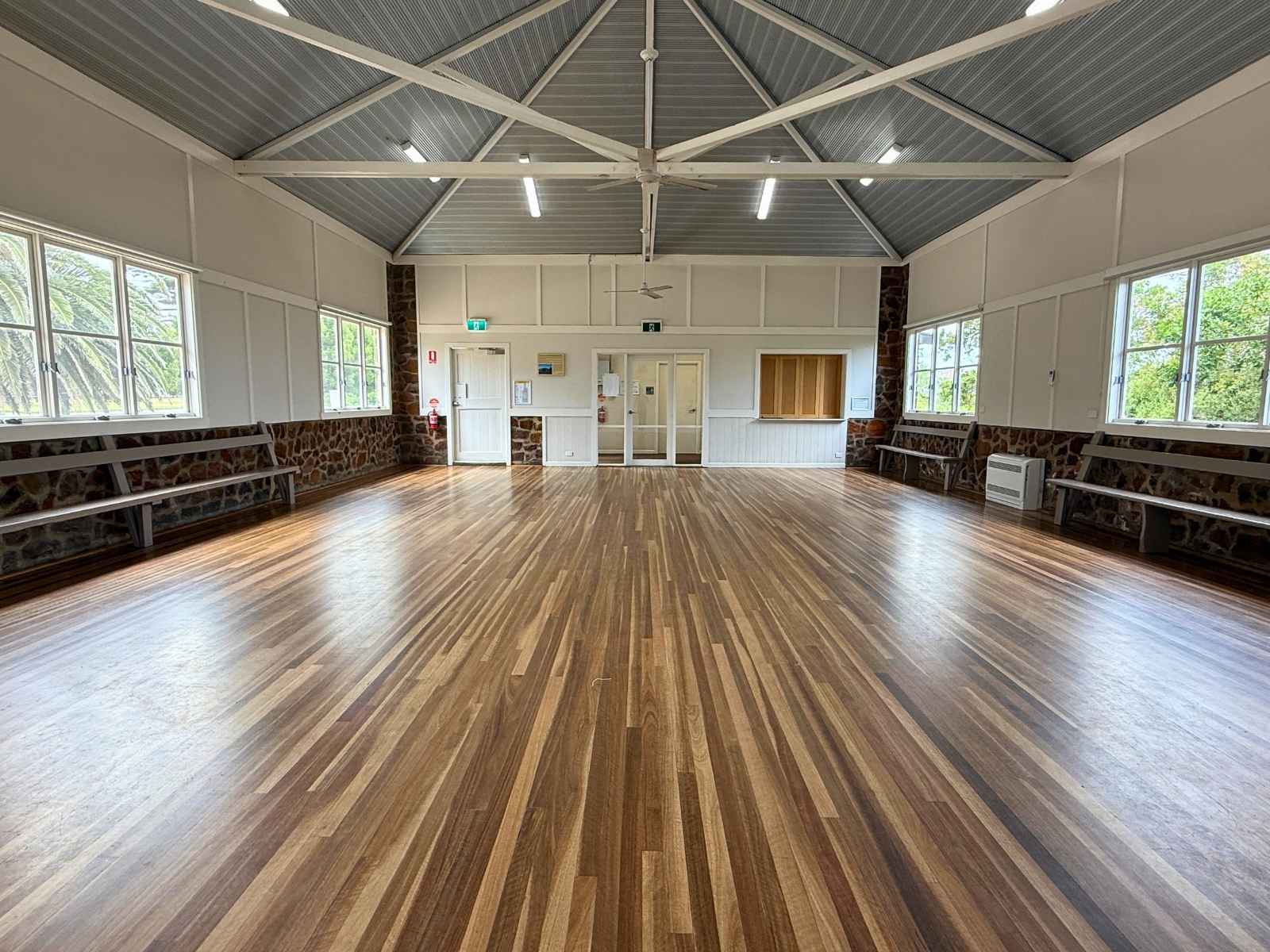 Wide-angle view of the empty hall interior, highlighting polished timber floors, stone base walls, and bright white panelling with ample natural light.