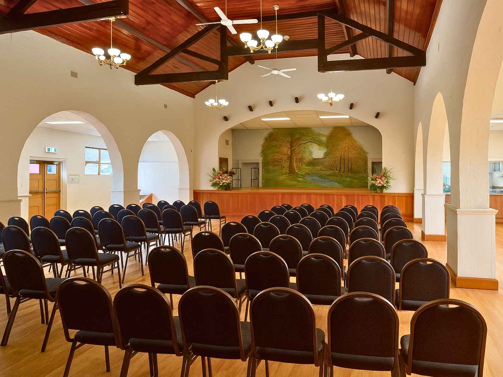 Somerville Mechanics Hall setup with rounded-back chairs facing stage with nature mural and arched doorways.