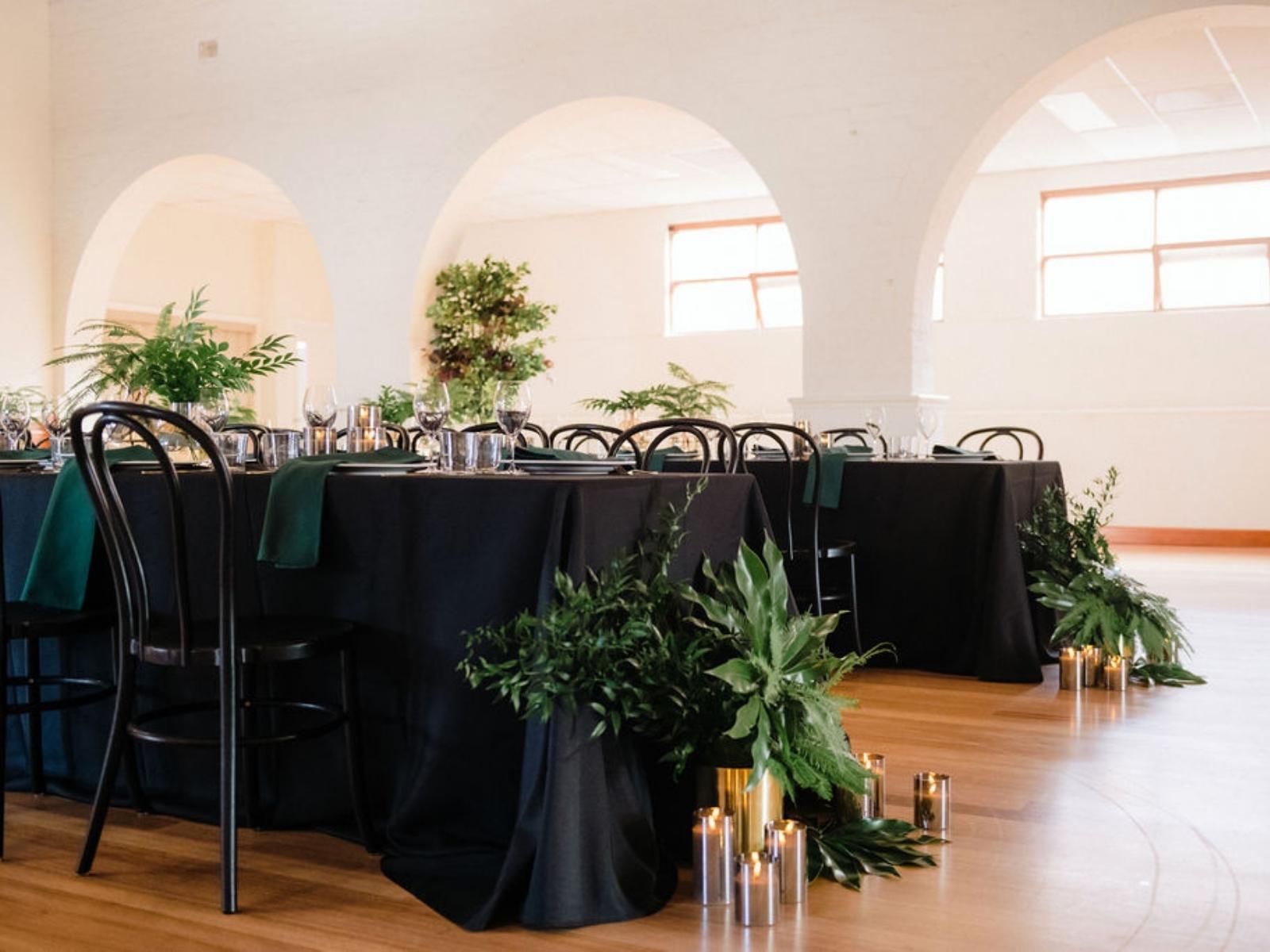 Detail view of Somerville Mechanics Hall dinner setting with lush green arrangements and candles near archways.