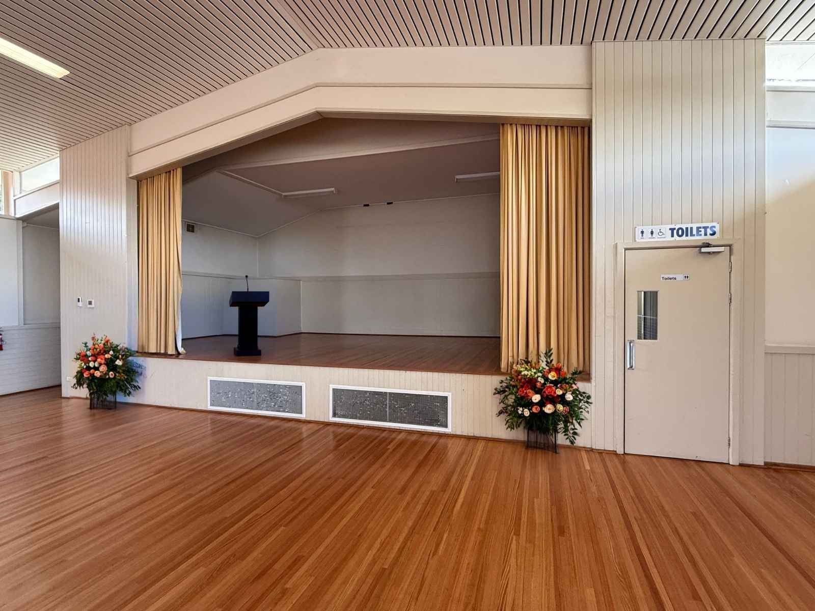 View of the Tyabb Community Hall stage with a black podium and floral arrangements on either side.