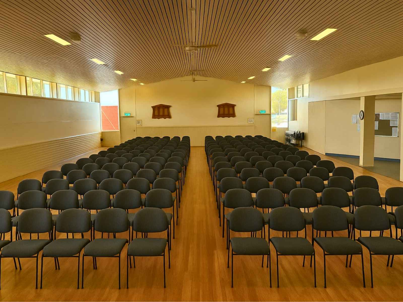 Rear view of evenly spaced grey chairs in Tyabb Community Hall, showcasing ample natural light from high windows.