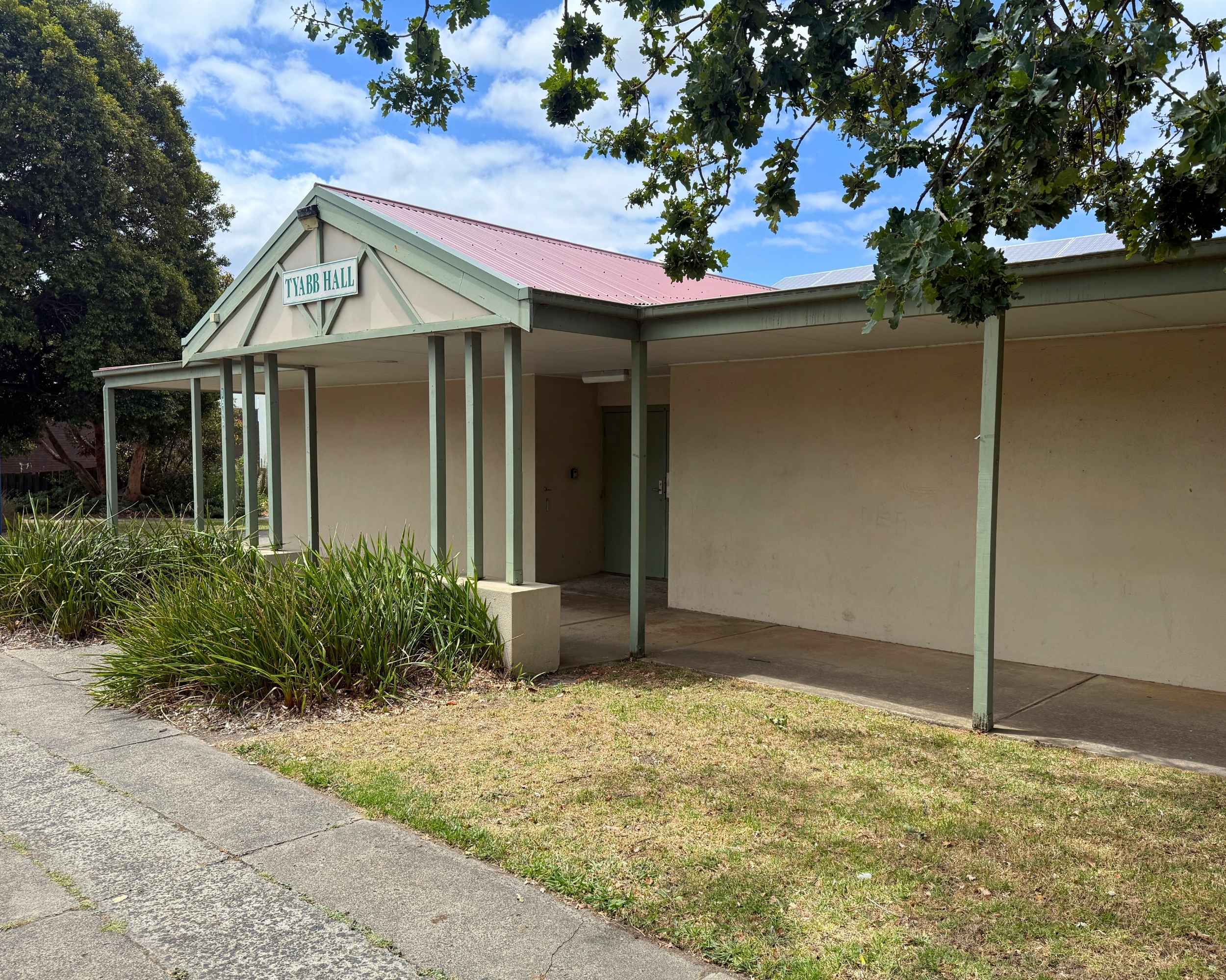 Exterior view of Tyabb Community Hall with a gabled roof and verandah, surrounded by greenery.