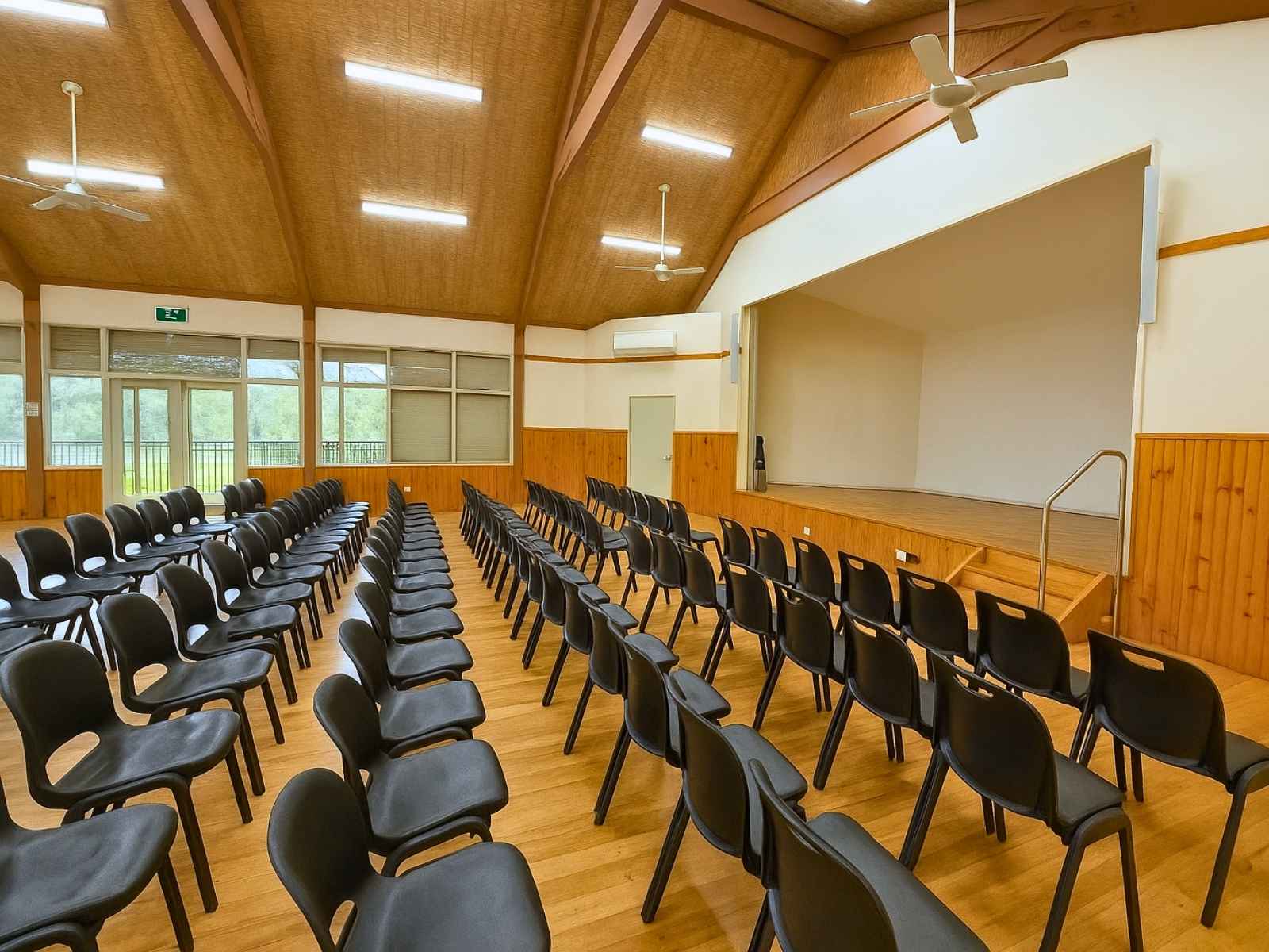 Interior of Main Ridge Community Hall set up with rows of black chairs facing a raised stage, ideal for ceremonies or performances.