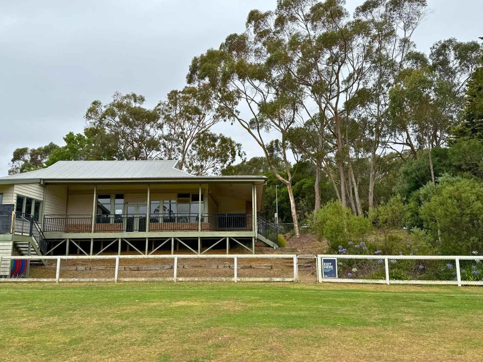 Rear view of Main Ridge Community Hall from across the oval, showing raised verandah, stairs, and surrounding native trees.
