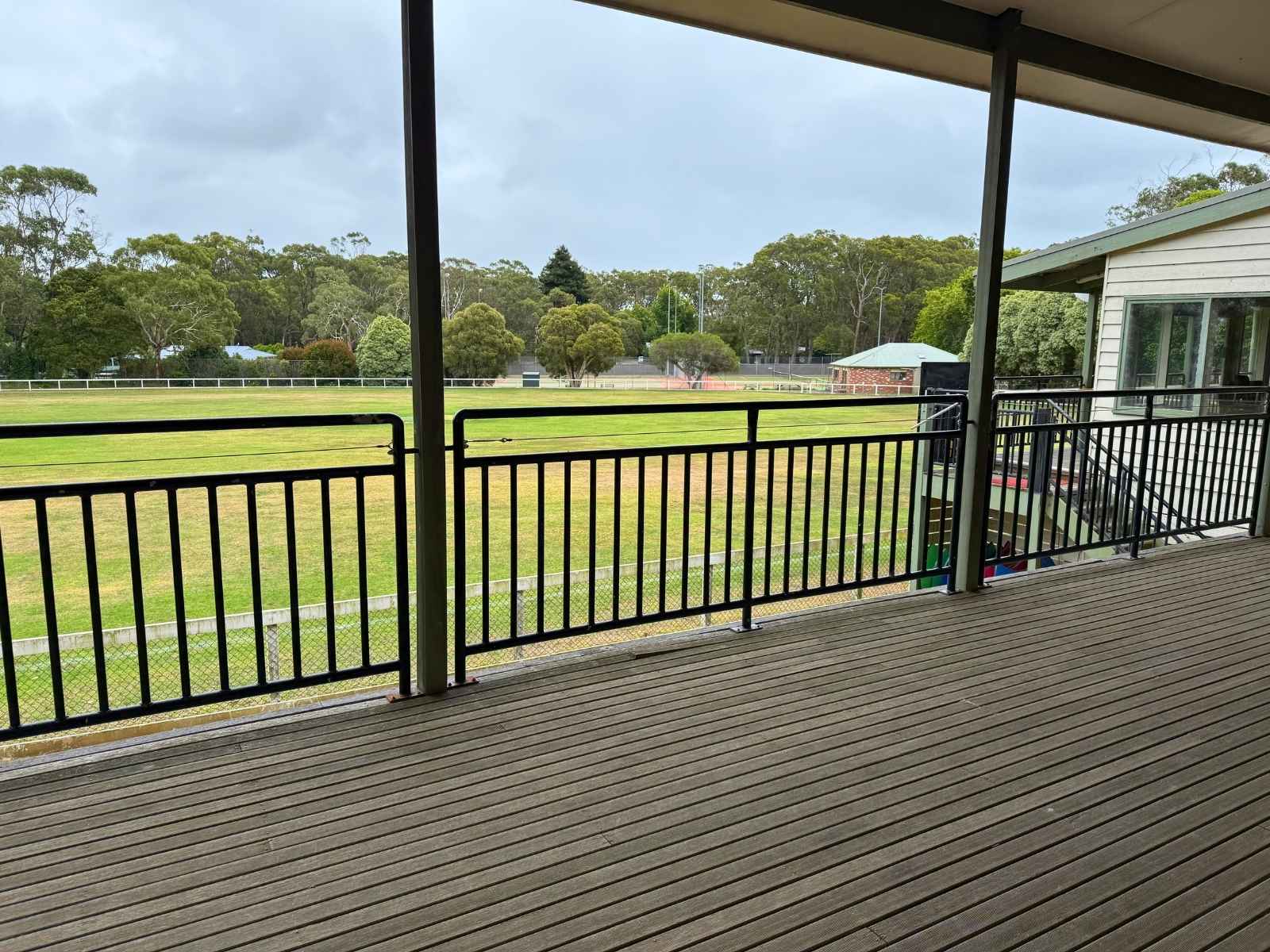 Outdoor covered deck at Main Ridge Community Hall overlooking a large grassy oval, ideal for informal gatherings or refreshments.