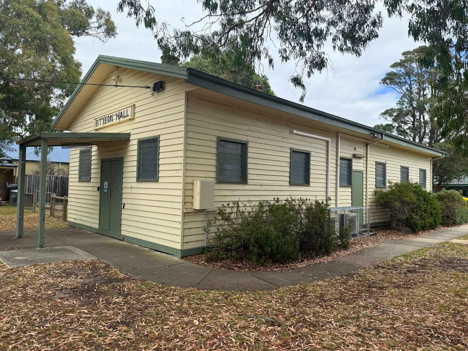 Side exterior of Bittern Hall, displaying timber weatherboard cladding, green doors, and accessible pathway.