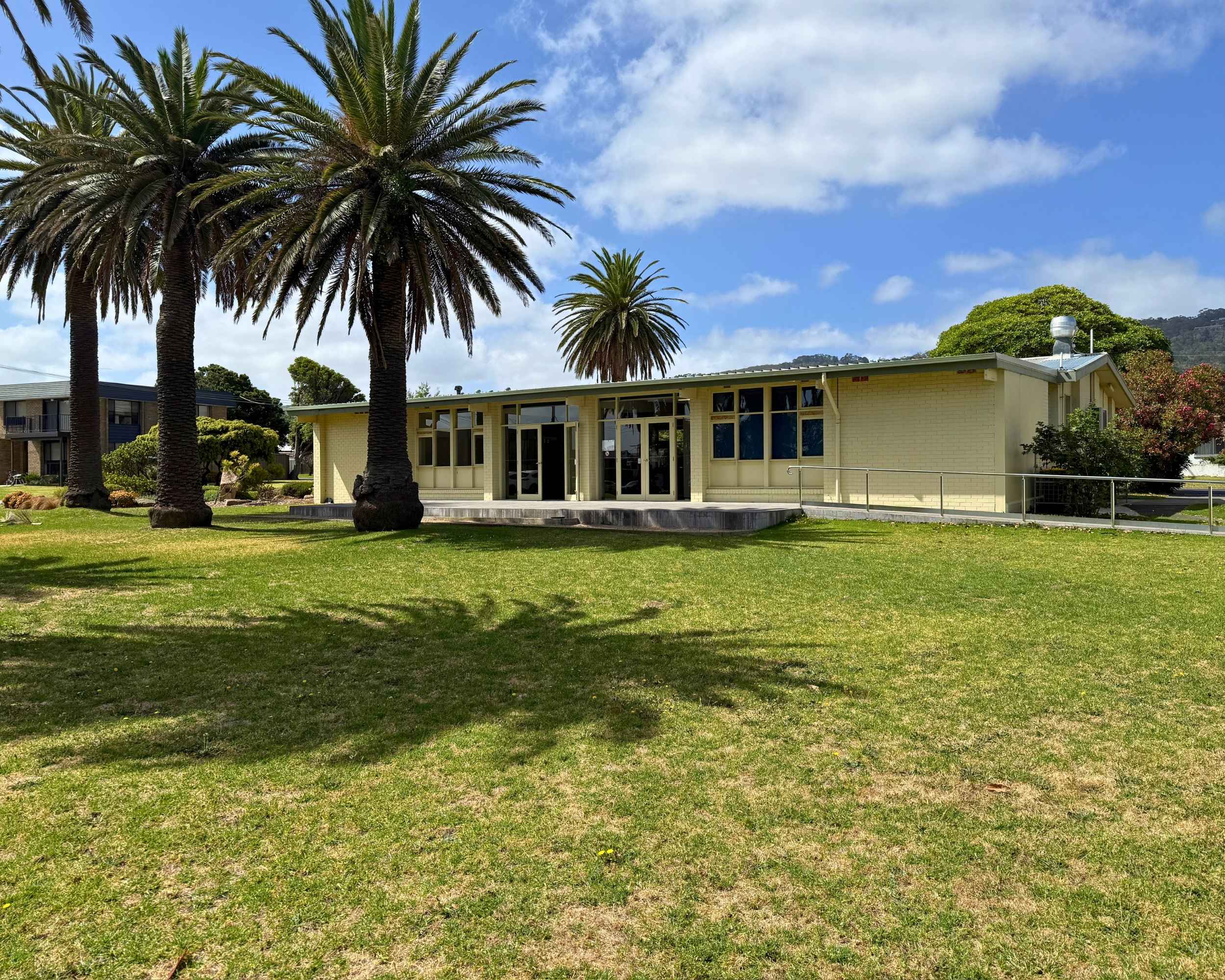 The hall is surrounded by open lawns and tall palm trees under a blue sky.