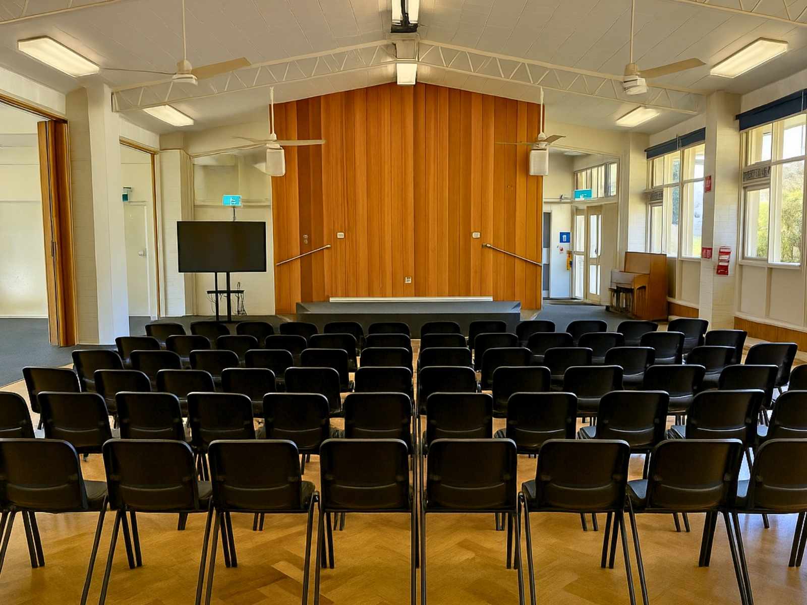 Large windows fill the room with light, facing a wooden stage with central access stairs.