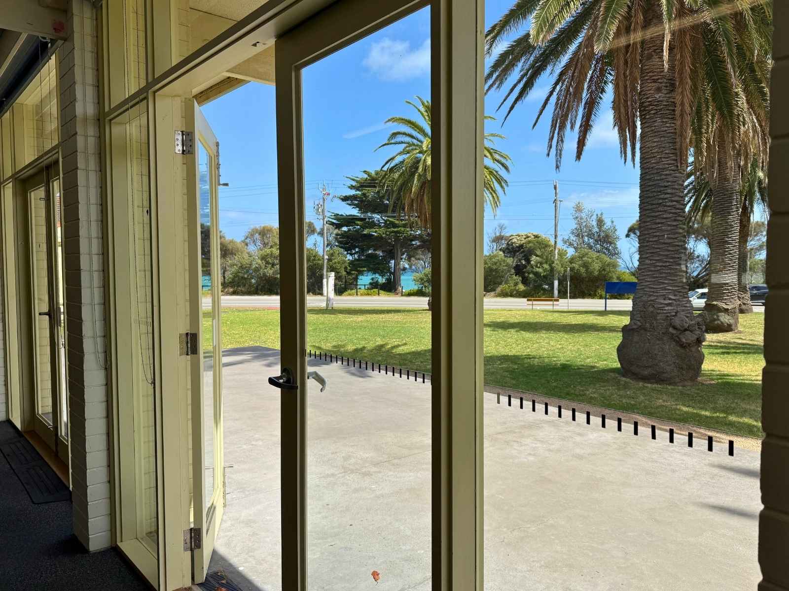 A view from inside the hall through glass doors to palm trees and a glimpse of the ocean beyond.