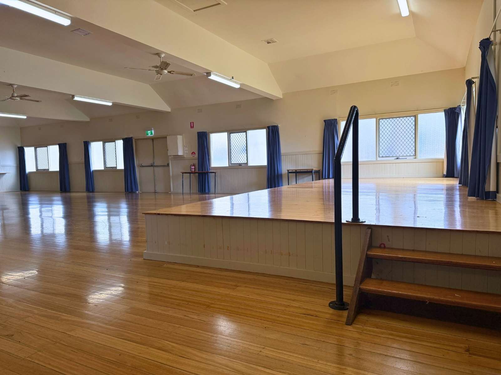 Raised timber stage with side steps and handrail, surrounded by open floor space and high windows.