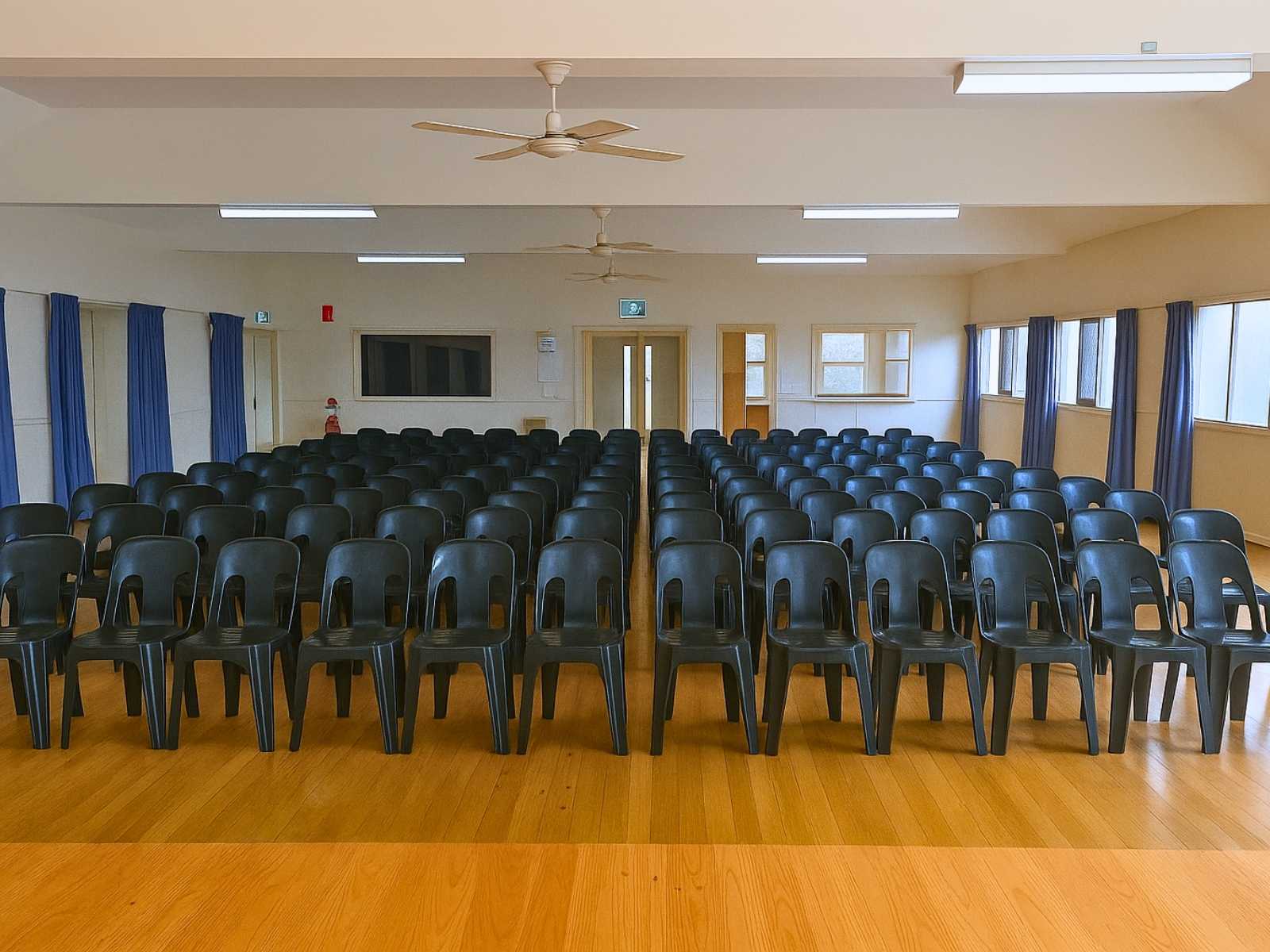 Audience-facing stage setup with rows of black plastic chairs and soft overhead lighting.