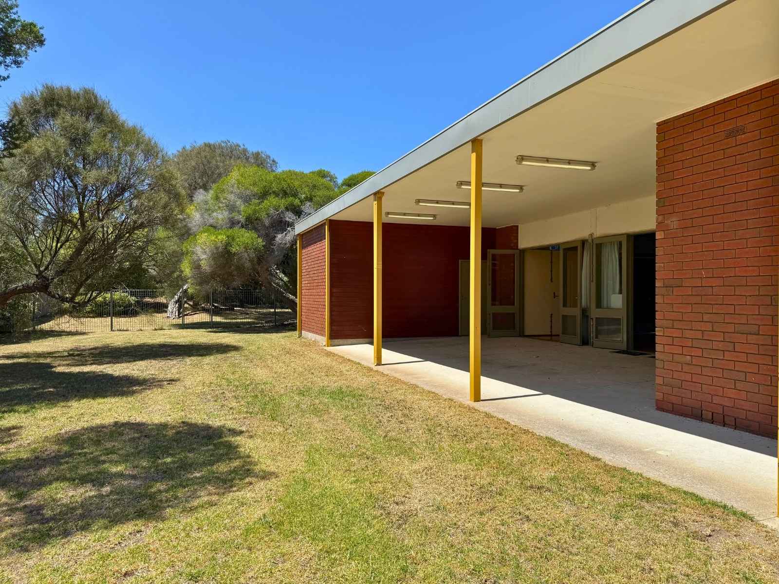 Outdoor covered area alongside the hall with yellow posts and surrounding greenery.
