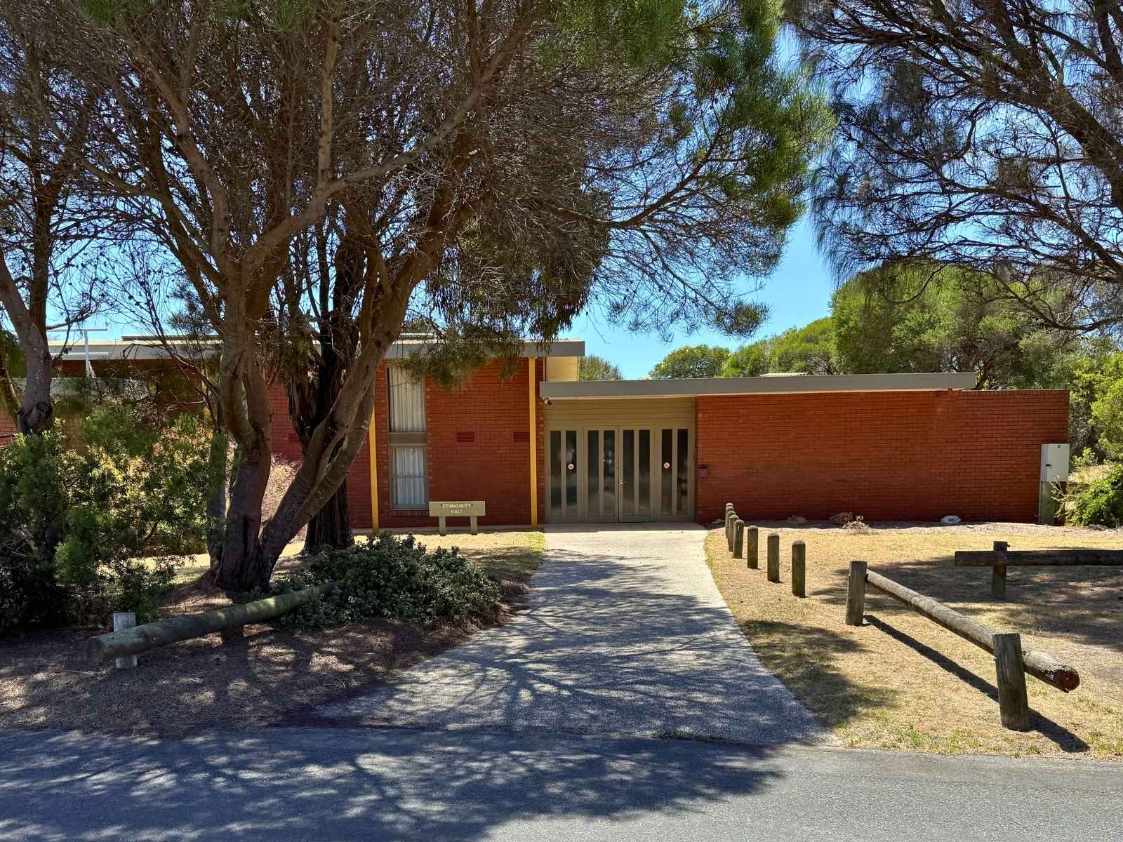 Wider exterior shot of the hall from the street, framed by tall coastal trees.