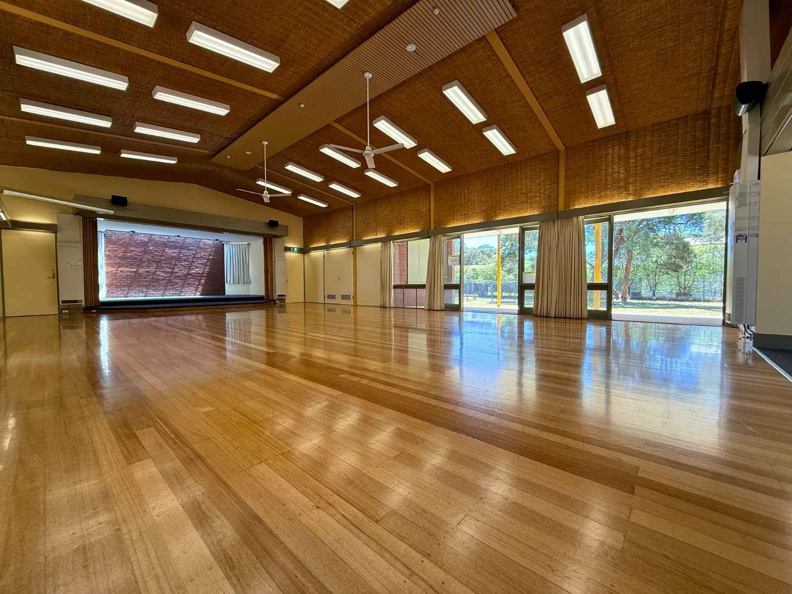 Empty main hall with stage and large windows letting in natural light, showcasing the open floor space.